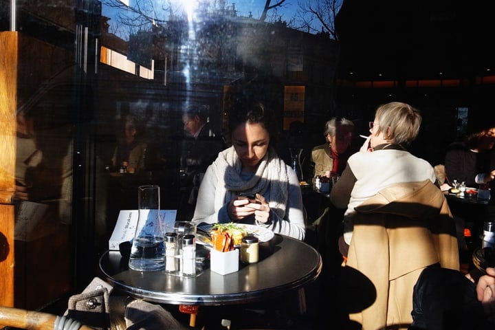 The best bistros for eating alone in Paris, like this cozy place where a woman is taking a picture of her food, as seen through the window.
