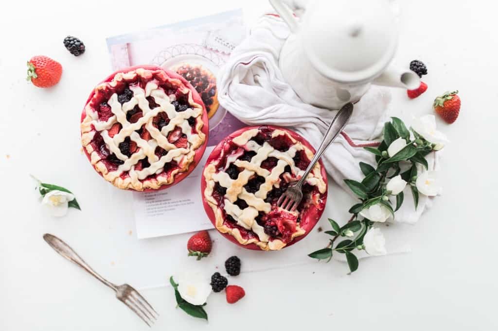 Two small cranberry pies sitting on a white table, garnished with berries and white flowers.