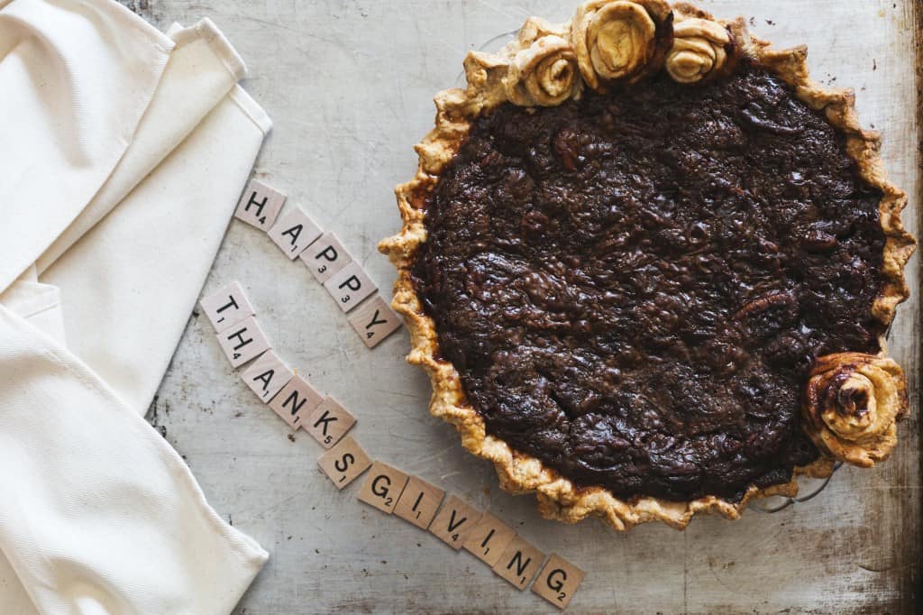 A brown pie on a marbled table with Scrabble letters used to express 'Happy Thanksgiving'.