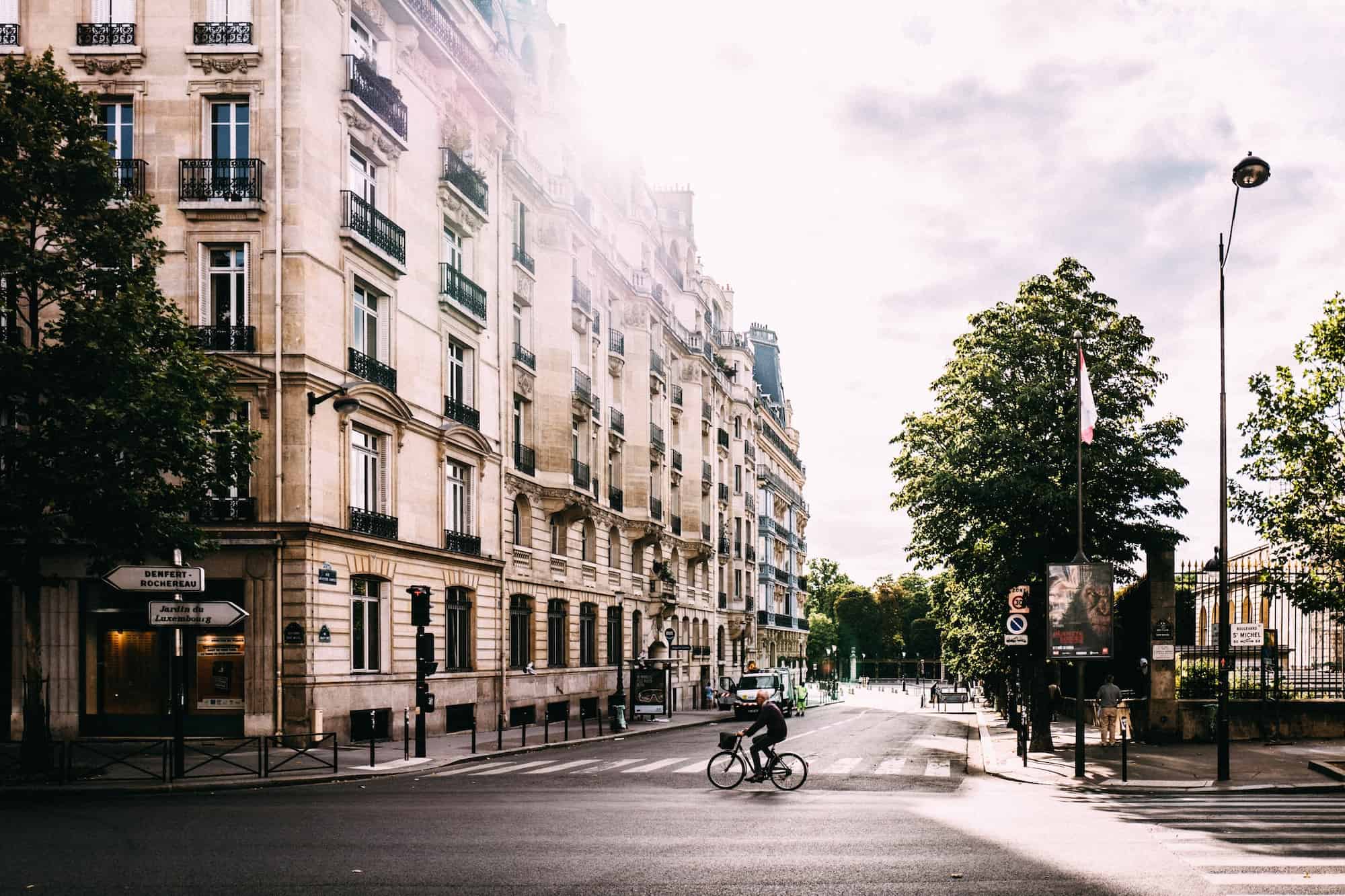 Contribute stories about living in Paris and photos like this picture of a man cycling through the sunny streets of Paris lined by Haussmann buildings and trees, in summer.