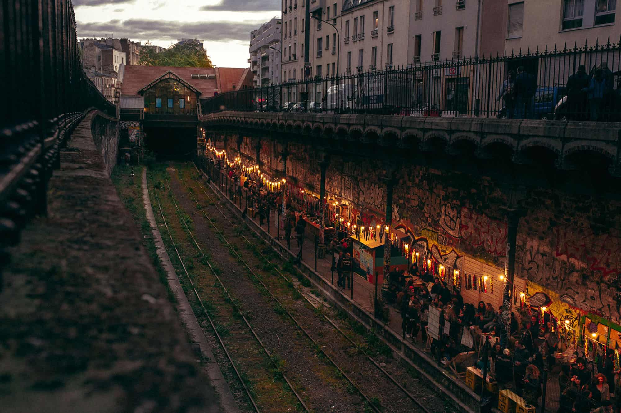 View of the Hasard Ludique bar with its outdoor summer terrace in Paris covered in graffiti on the old platform of an abandoned train station.
