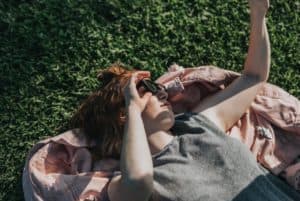 A young red-haired woman lying down on the grass, wearing sunglasses and tanning in a park in Paris.