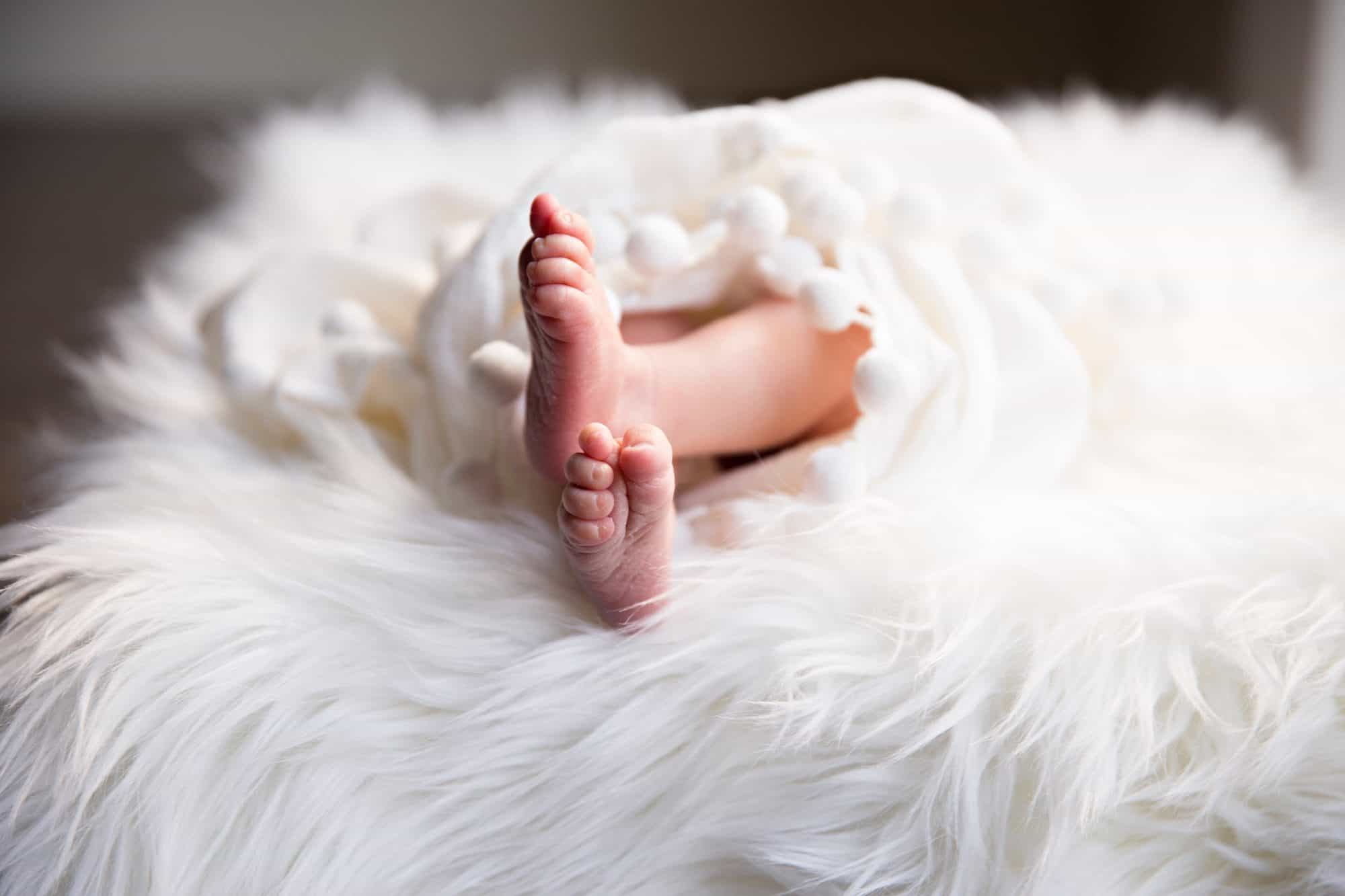Tiny cute new-born baby feet sticking out of a fluffy rug.