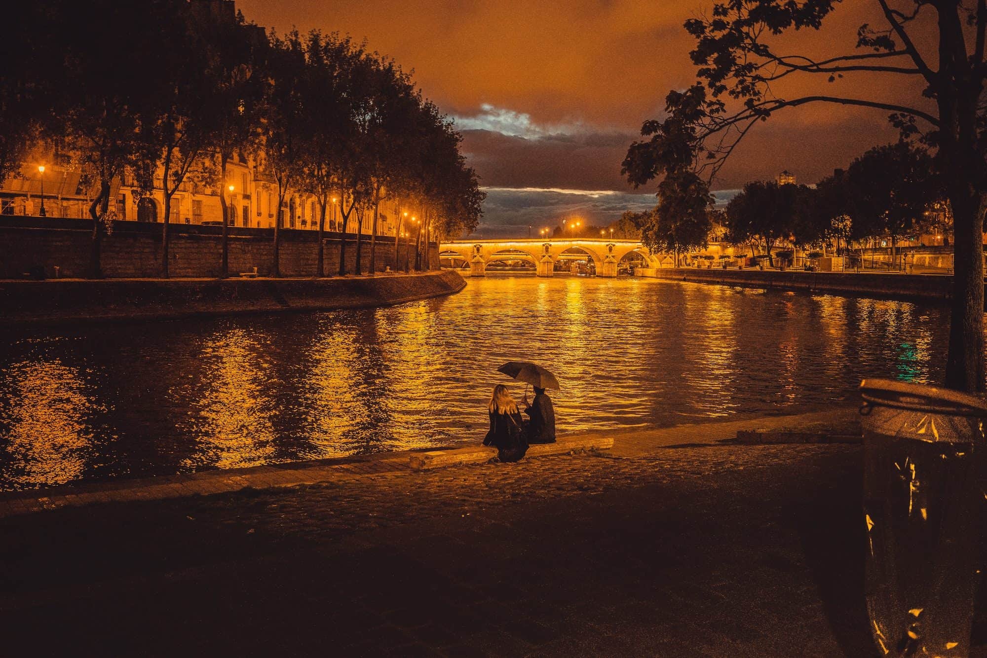A couple having a date in the rain, sitting on the banks of the River Seine.