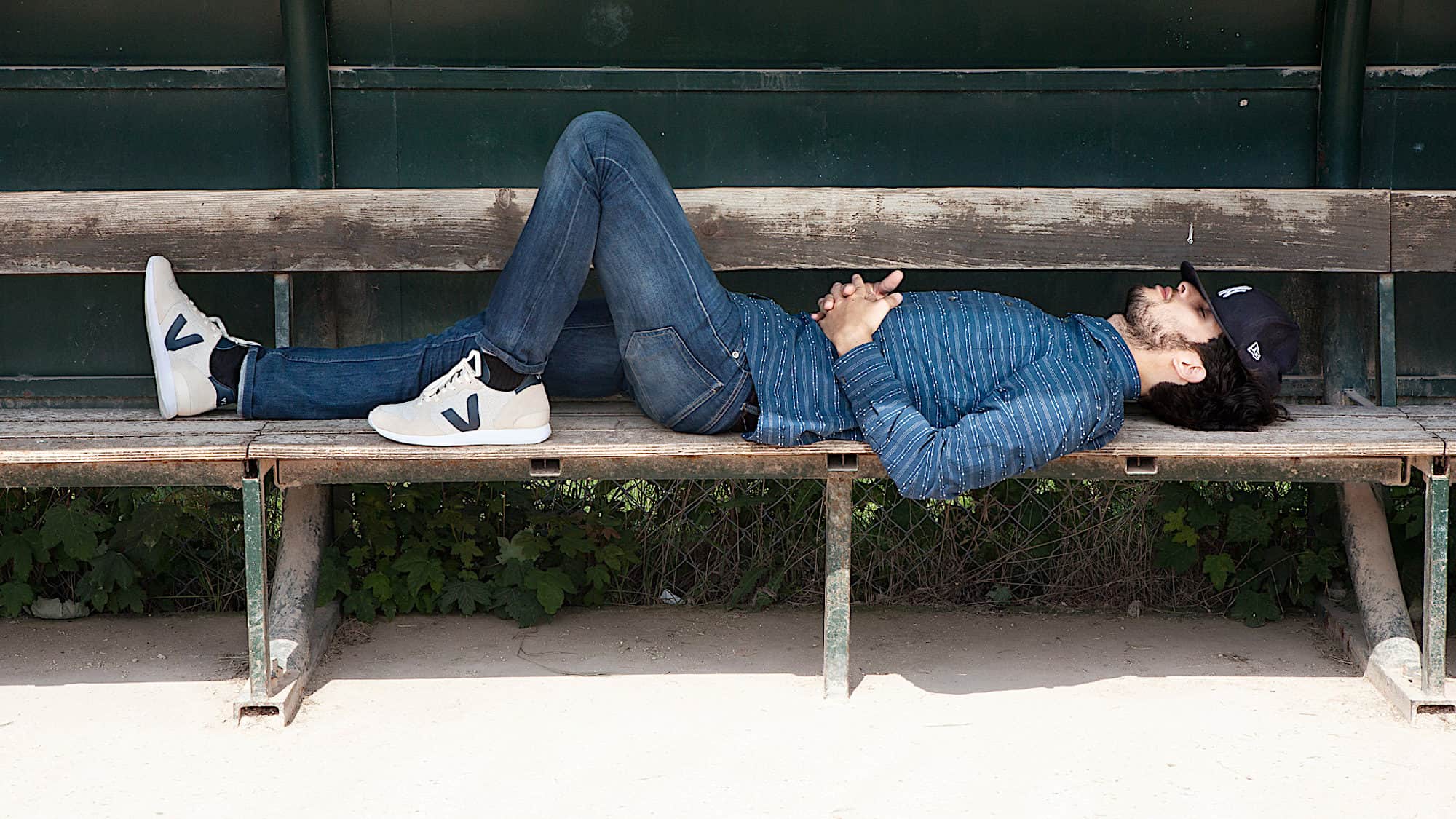 Sustainably made Veja trainers are also go-tos for Parisian men, like this young man wearing jeans and blue shirt, lying on a bench sleeping.