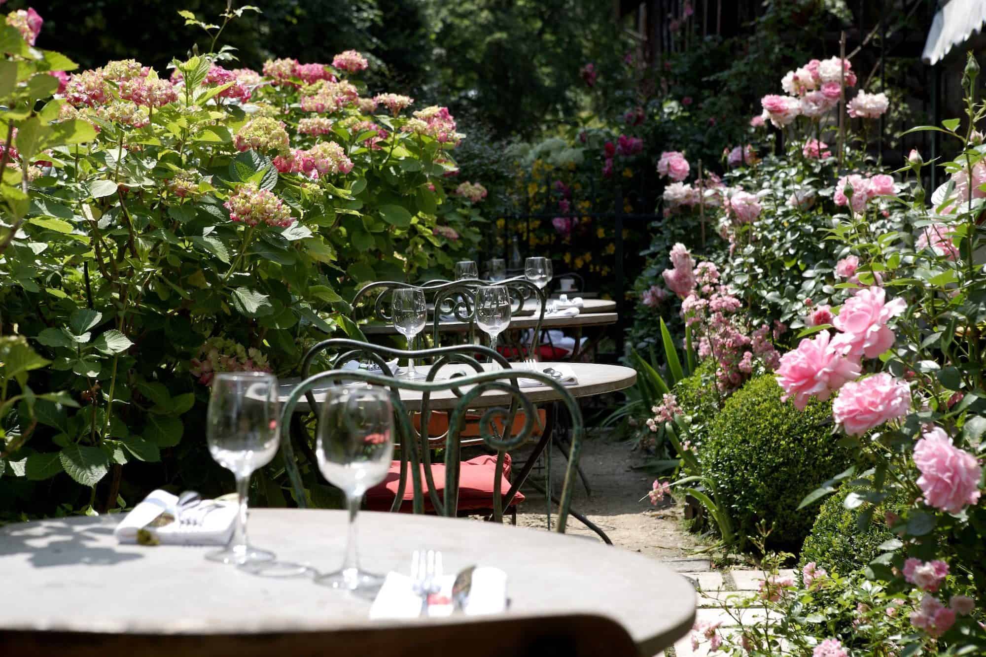 Les Etangs de Corot Hotel garden with tables slotted among the pink rose bushes.