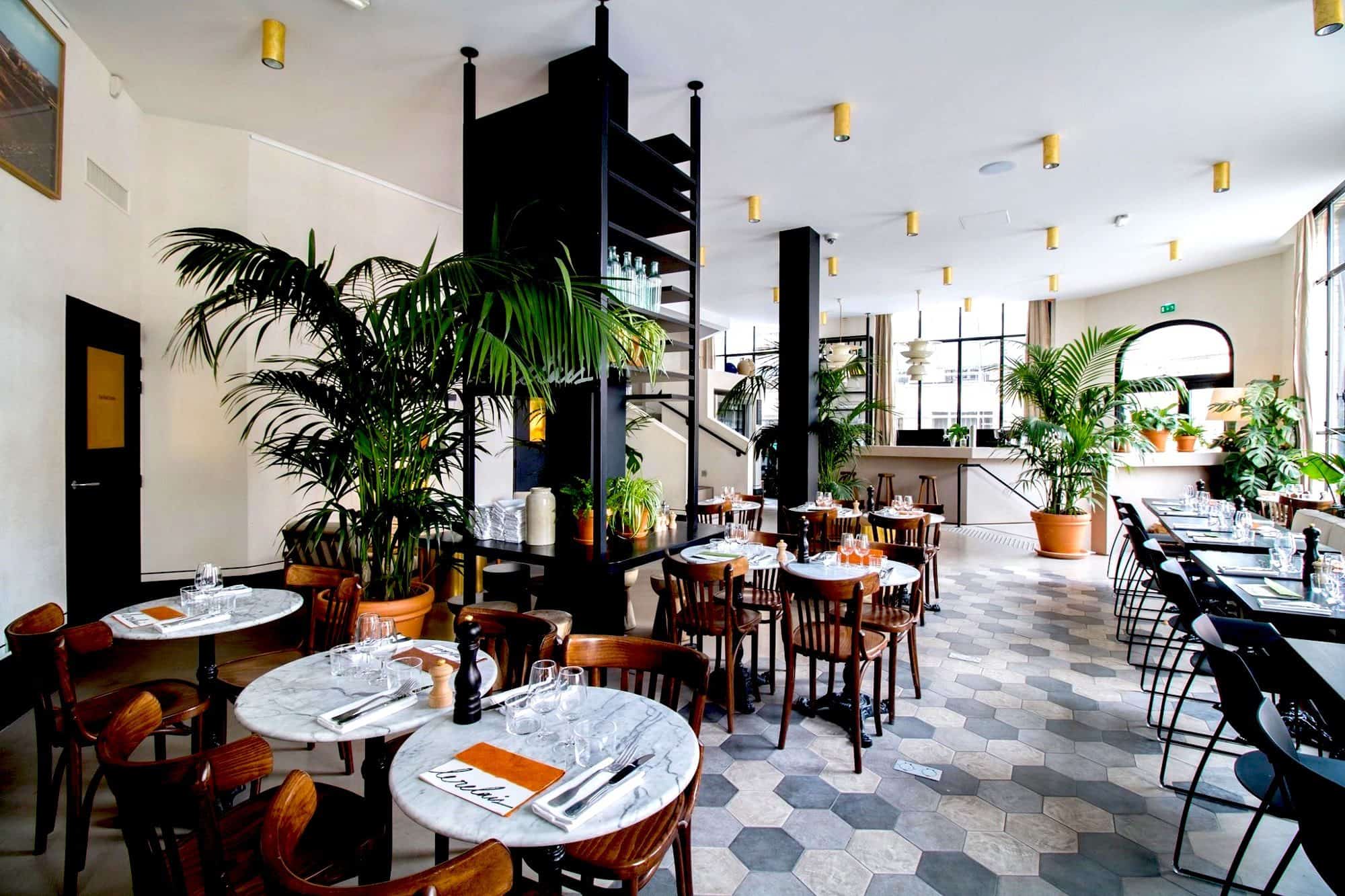 The main dining space at Le Relais restaurant in Paris, a light and bright space with potted plants and tiled floors.