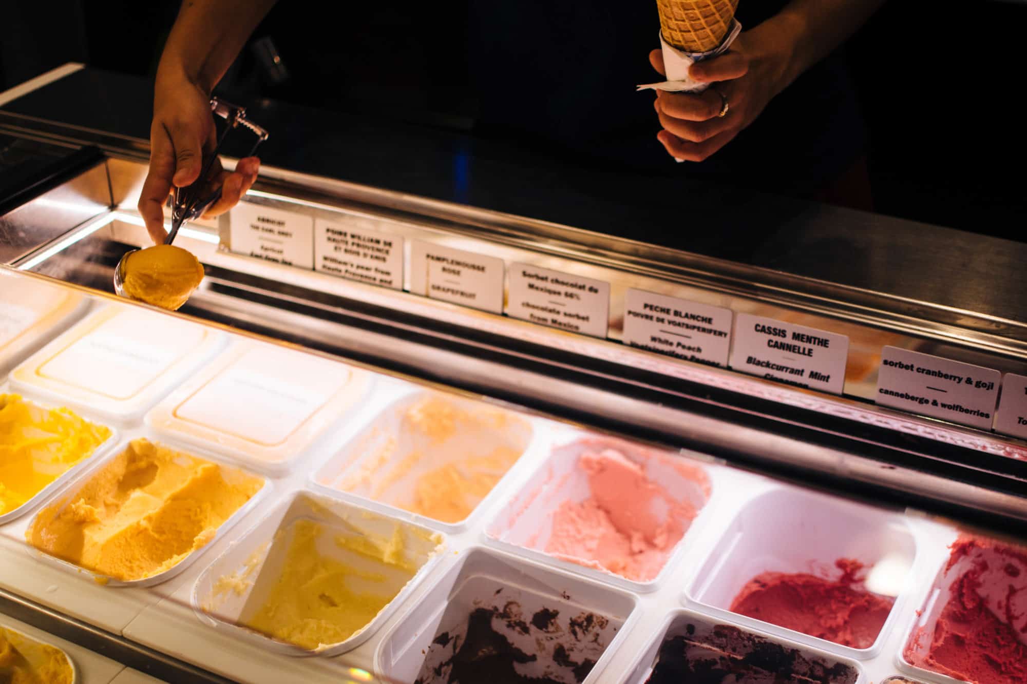 The ice cream counter at Pozzeto ice cream shop in Paris with a vendor scooping out the flavors into a cone.