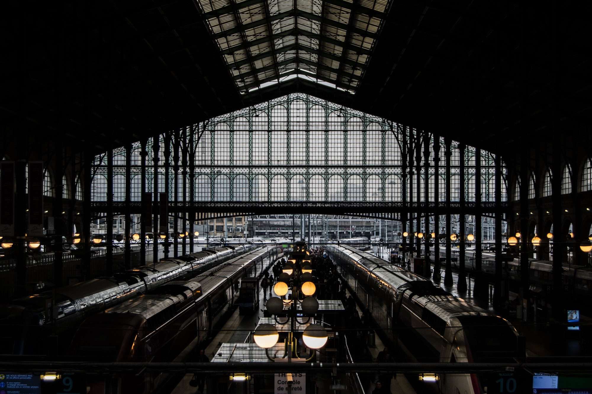 A shadowed view of trains waiting at the platforms of the Gare du station with its Art nouveau glass and iron structure.