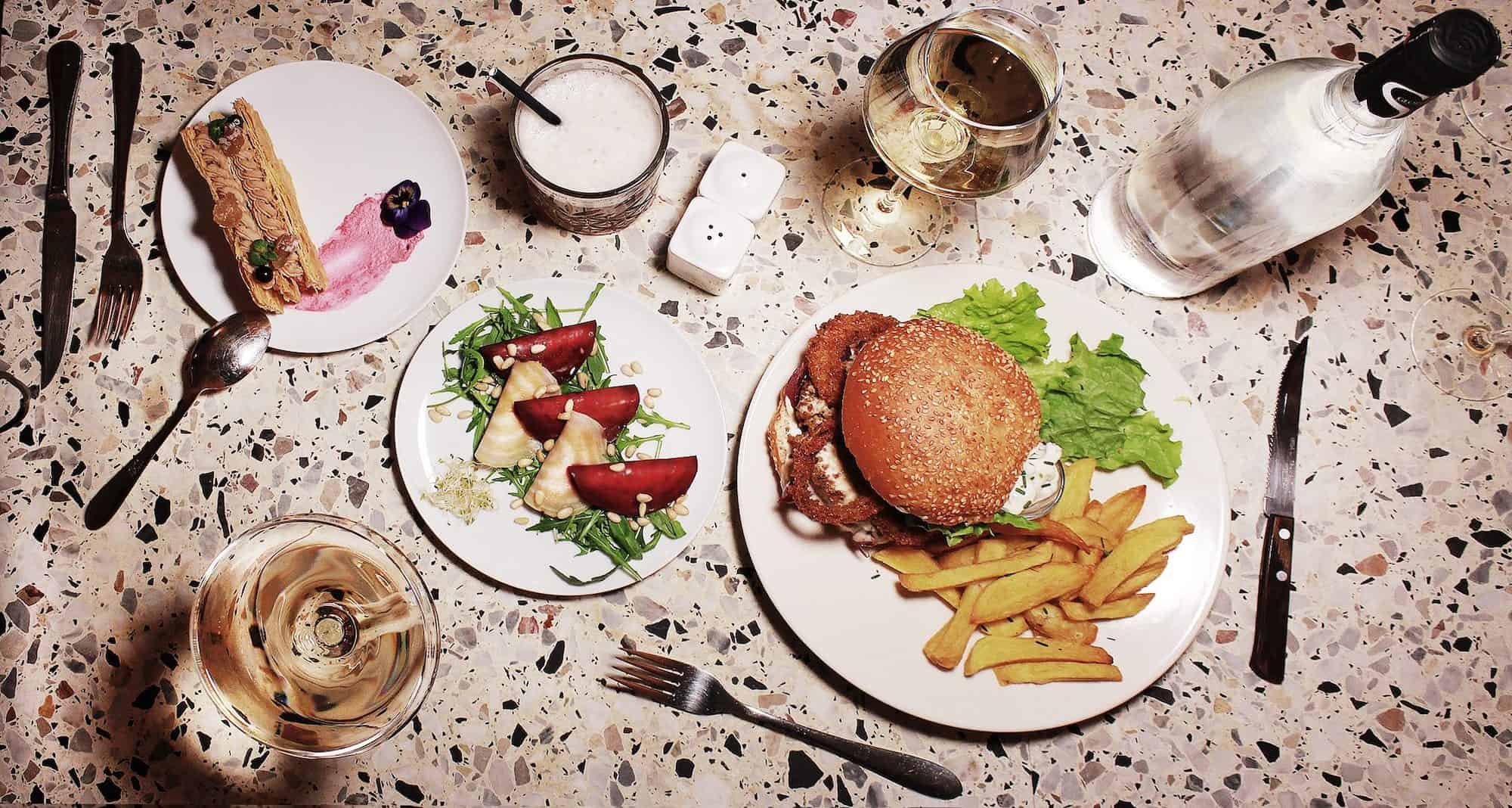 A spread of vegan burger with homemade fries and a starter of beetroot on a terrazzo table at BrEAThe restaurant in Paris.