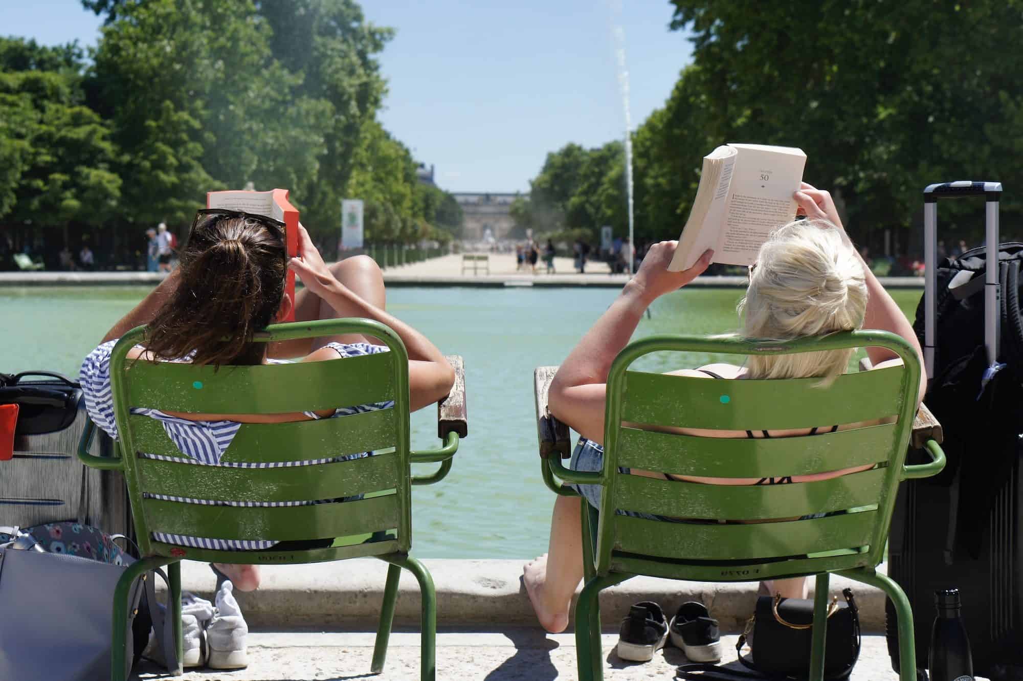 Two women leaning back in chairs by the water feature at the Jardin des Tuileries in Paris while reading books in the sunshine. They probably said "bonjour" even if they don't know one another.