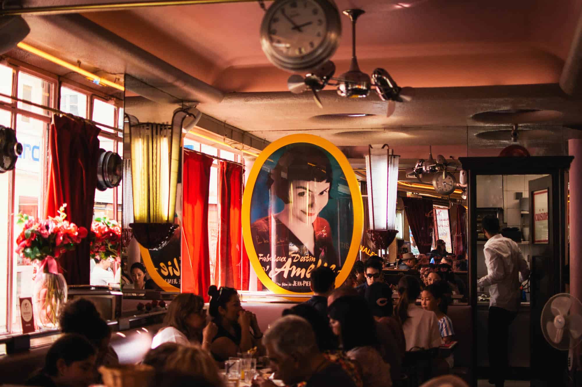 Inside the Café des 2 Moulins, otherwise known as the café in the movie "Amélie", with an image of Amélie printed on a glass pane and people sat in booths.