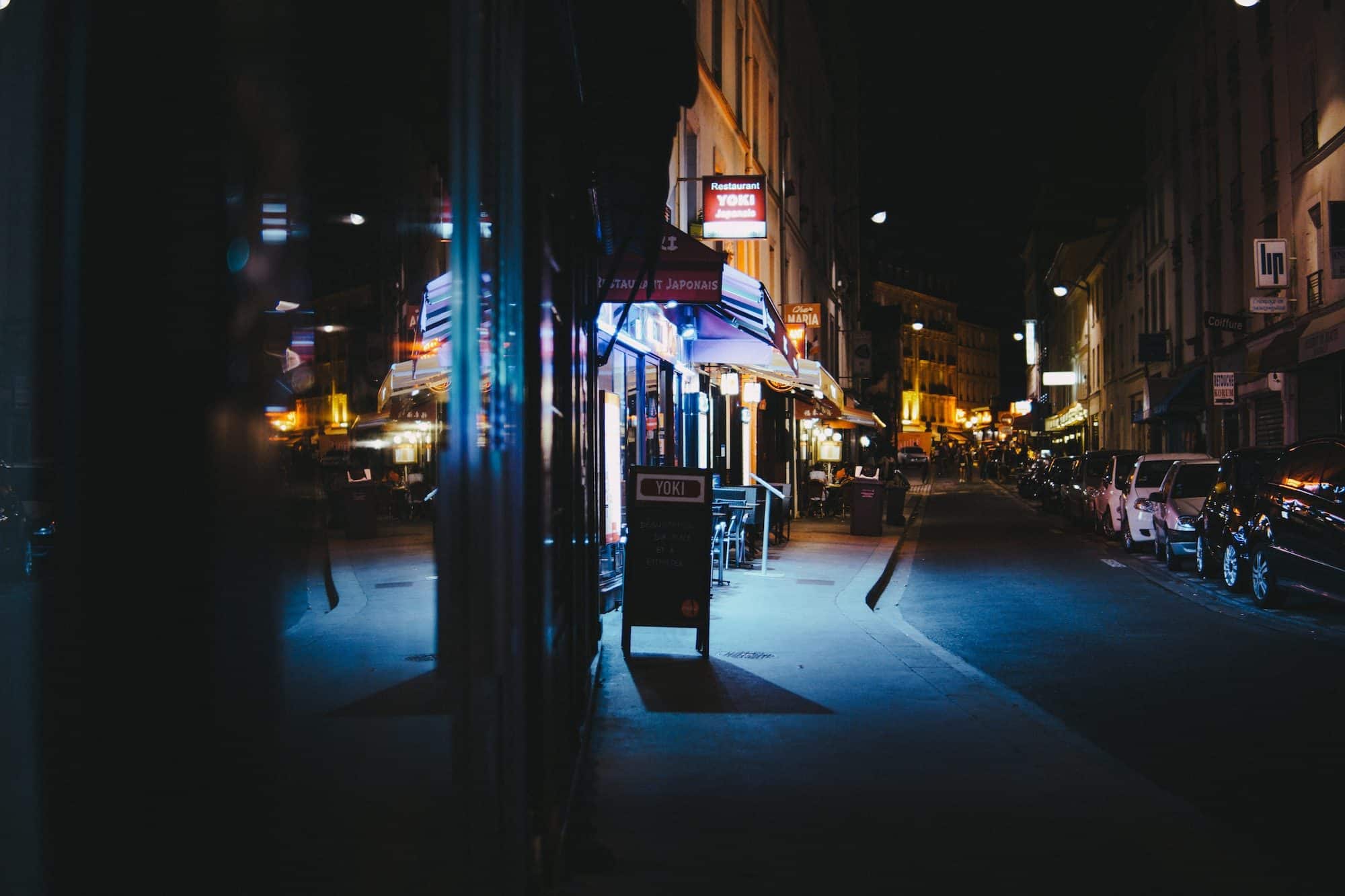 A night street scene in Paris of neon shop signs lining on empty street.