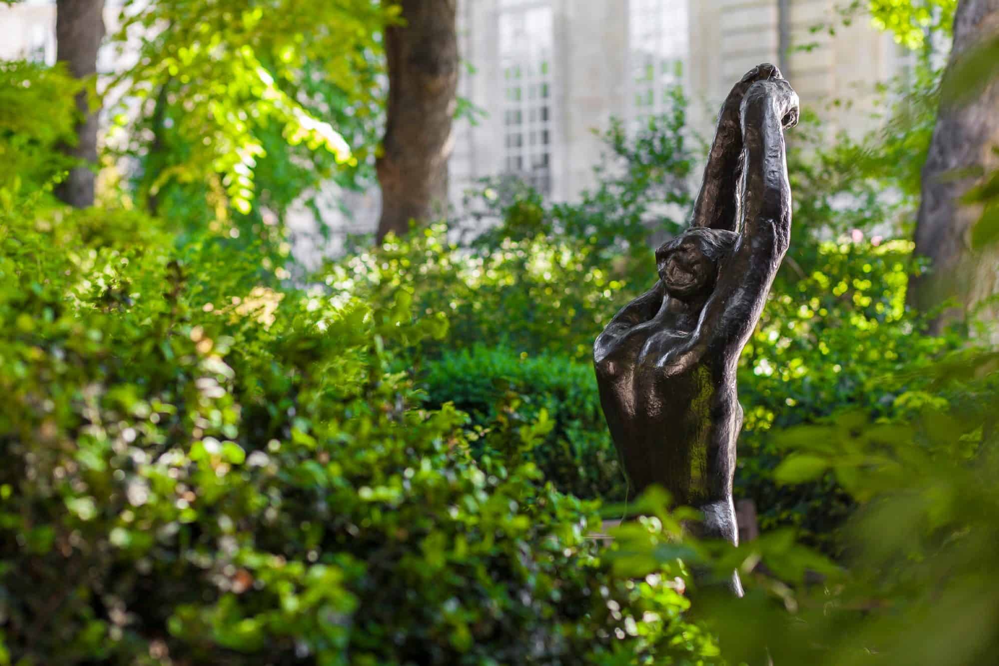 The Rodin Museum gardens with a sculpture of a woman her arms up among the foliage (right).