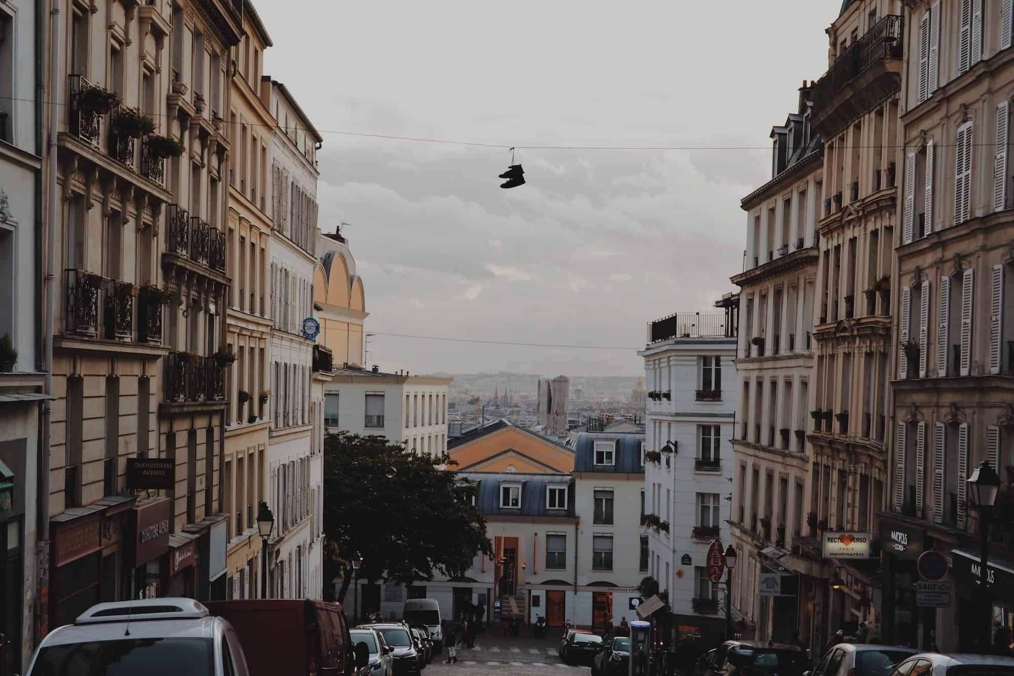 A street scene of Montmartre as the sun sets, which apartment buildings on either side and shoes hanging on street cables in the center. 