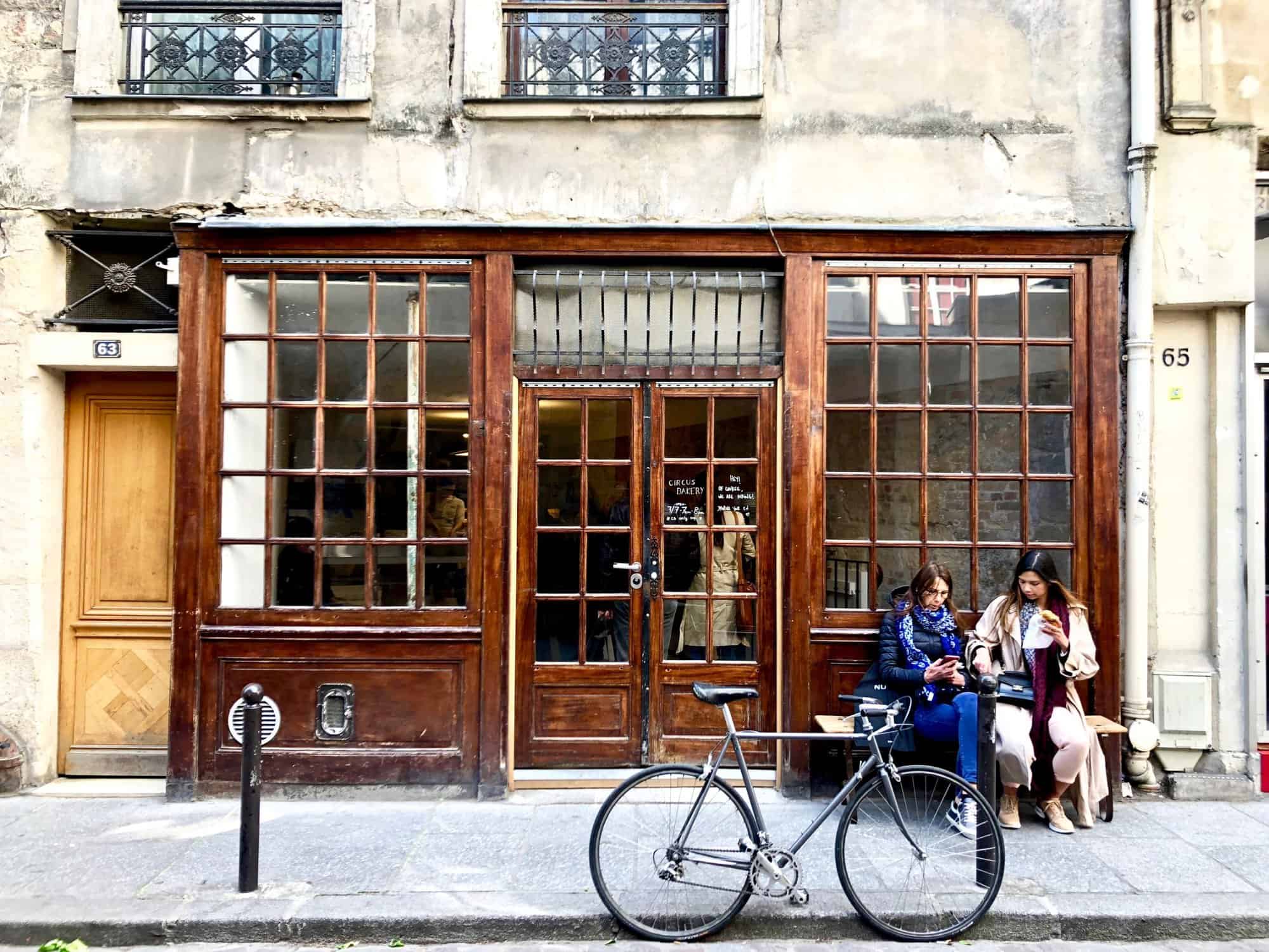 The old wooden exterior of Circus Bakery in Paris with two women sitting outside on a bench.