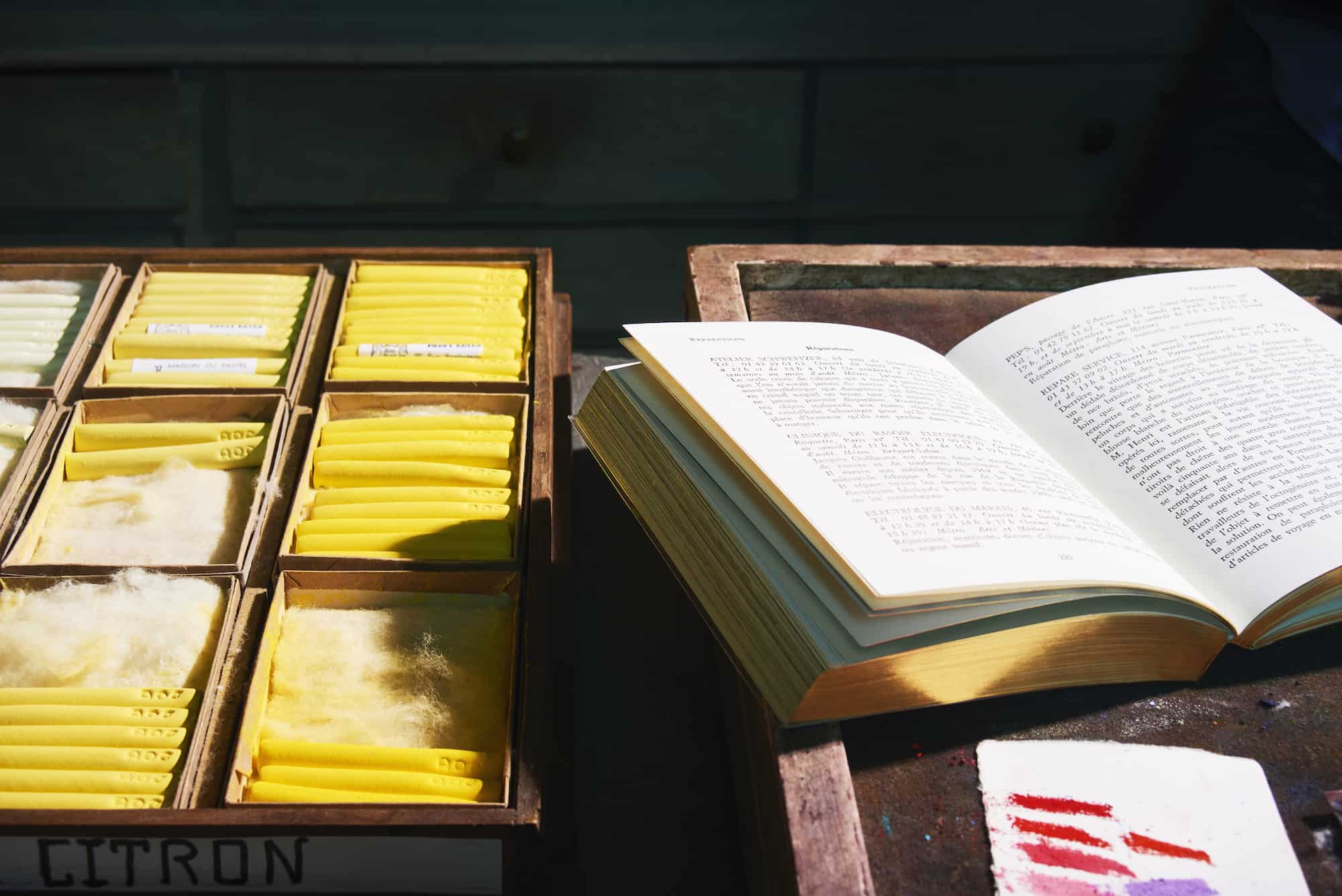 A book by Astier de Vilatte, with gold trim, opened on a wooden tray, outside in the sun.