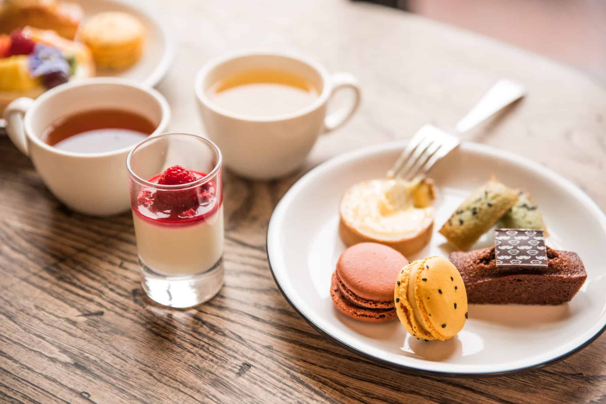 Macarons, a mini lemon tart, and financiers sit next to panna cotta and piping hot cups of tea.