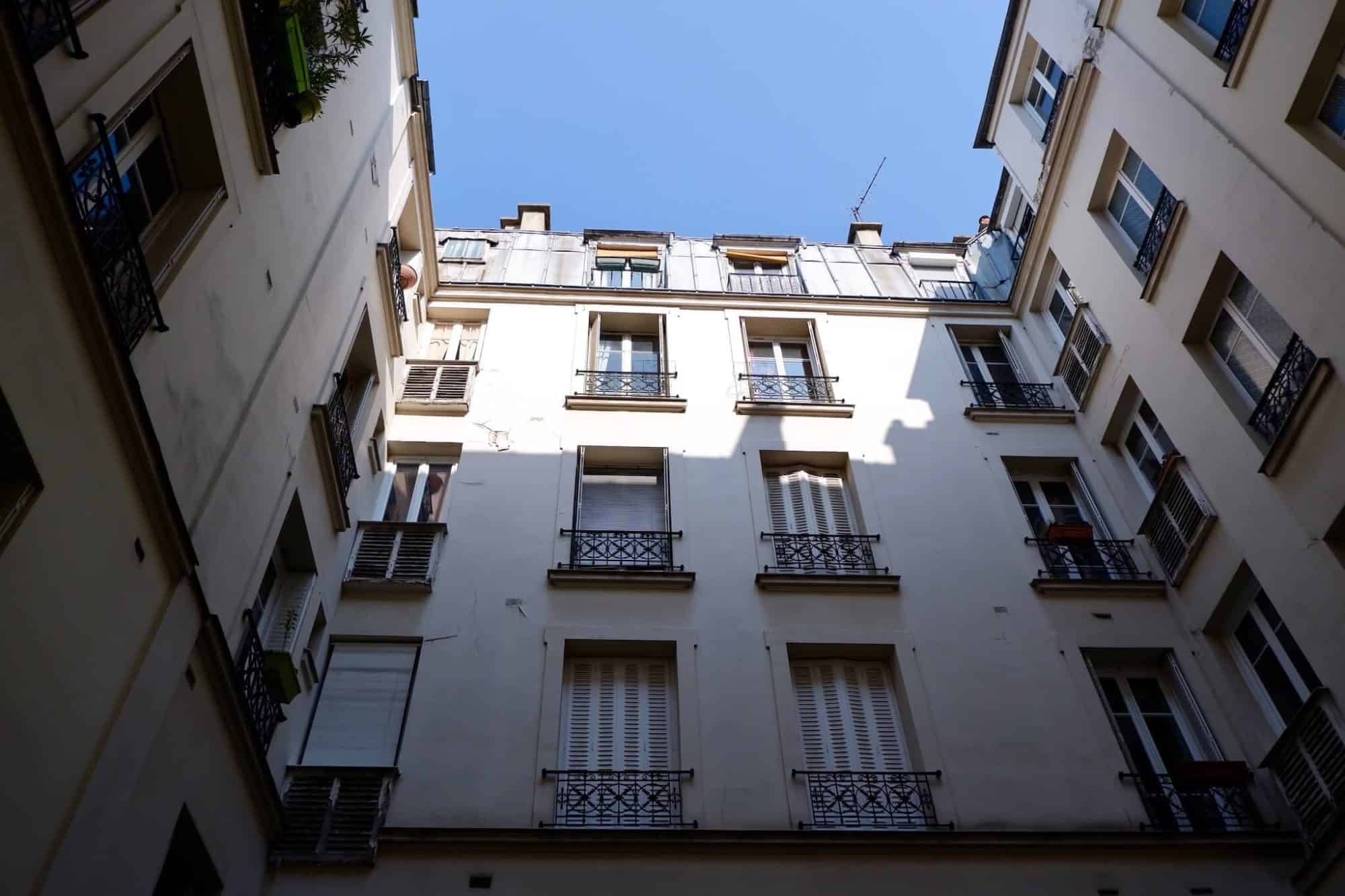 The courtyard view of Ali's Paris apartment, sunlight cast at the top of the building. 