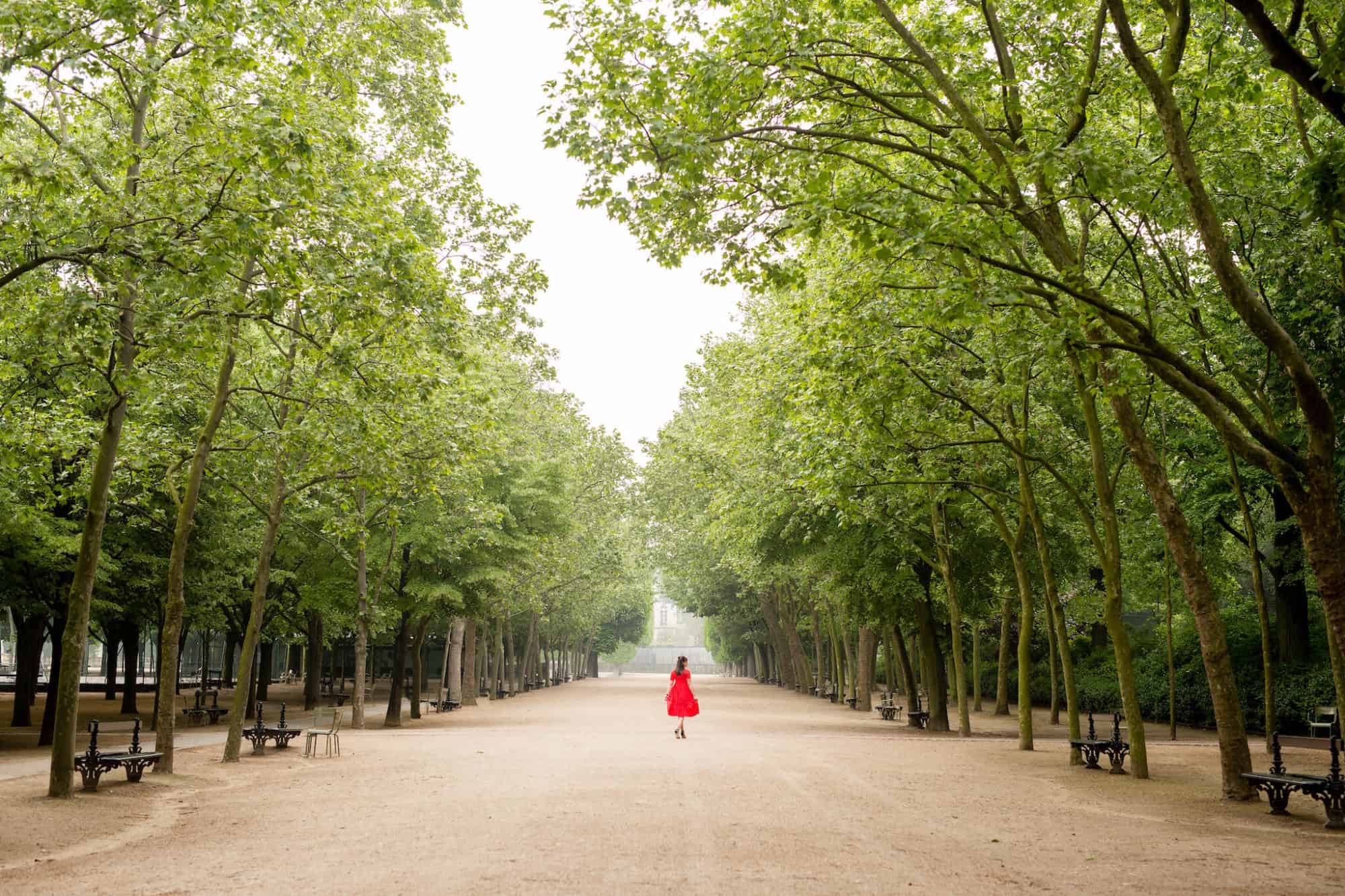 Rebecca Plotnick, travel photographer and blogger at Everyday Parisian, takes a twirl in an empty Tuileries garden, her bright red dress punctuating the verdant trees. 