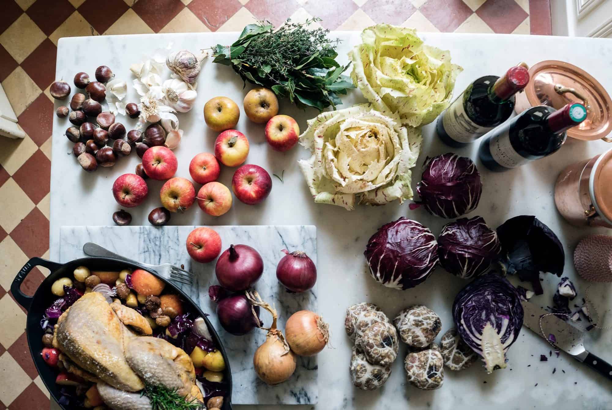 A sunlit-flooded table overflows with fresh produce: Leafy greens; chestnuts; a chicken to roast; apples; and, of course, wine. 