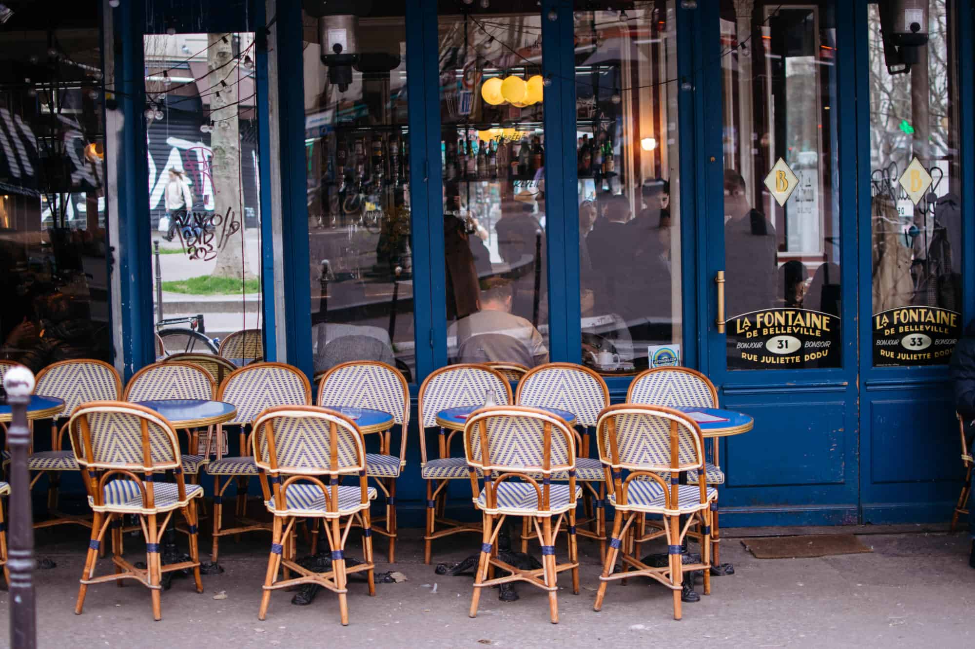 Café tables and chairs sit outside La Fontaine de Belleville, a french coffee shop in Paris' 10th arrondissement.