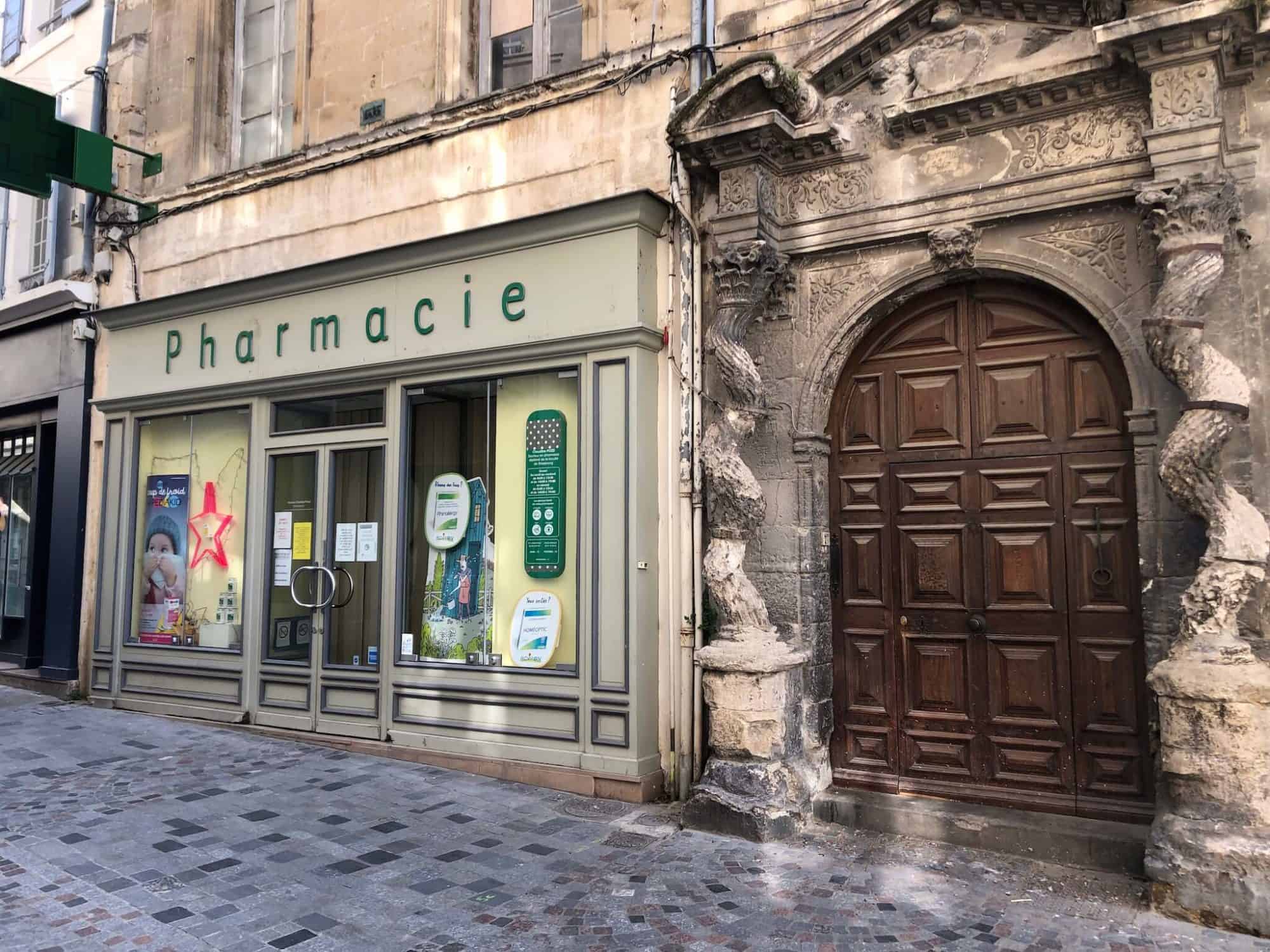 A pharmacie and door to a building on a street in Arles, France.
