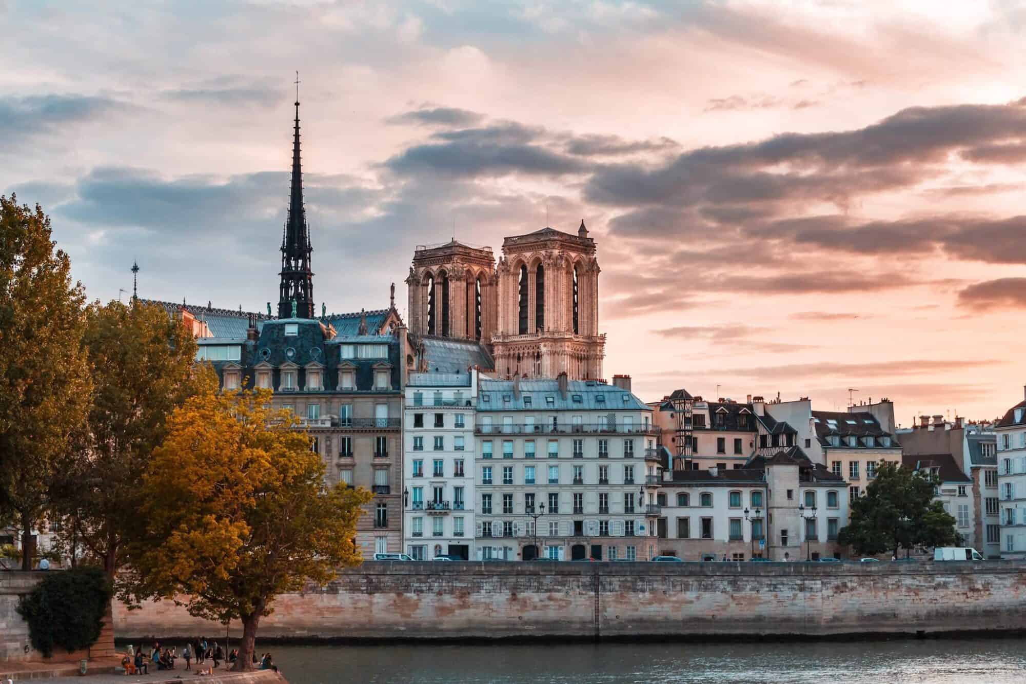 A view of Pont-Neuf, the Seine, Parisian apartments, and in the background, Notre-Dame, at sunset.