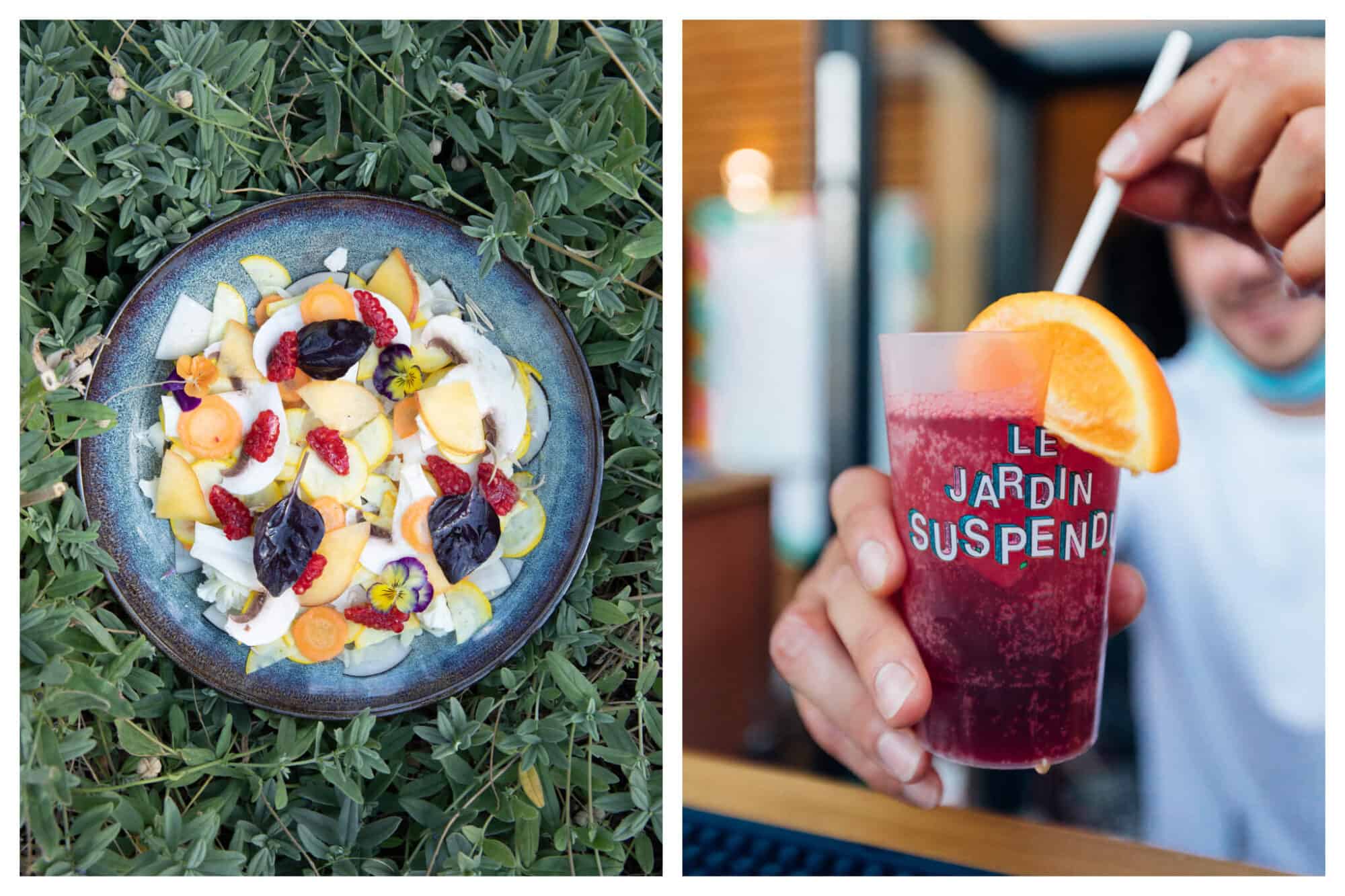 Left: a salad on a blue ceramic plate sitting on some greenery. The salad is colorful, with orange, yellow, red and purple. Right: a red cocktail in a plastic cup with a slice of orange and a straw, held by the bartender. The cup has the words Le Jardin Suspendu on it. 