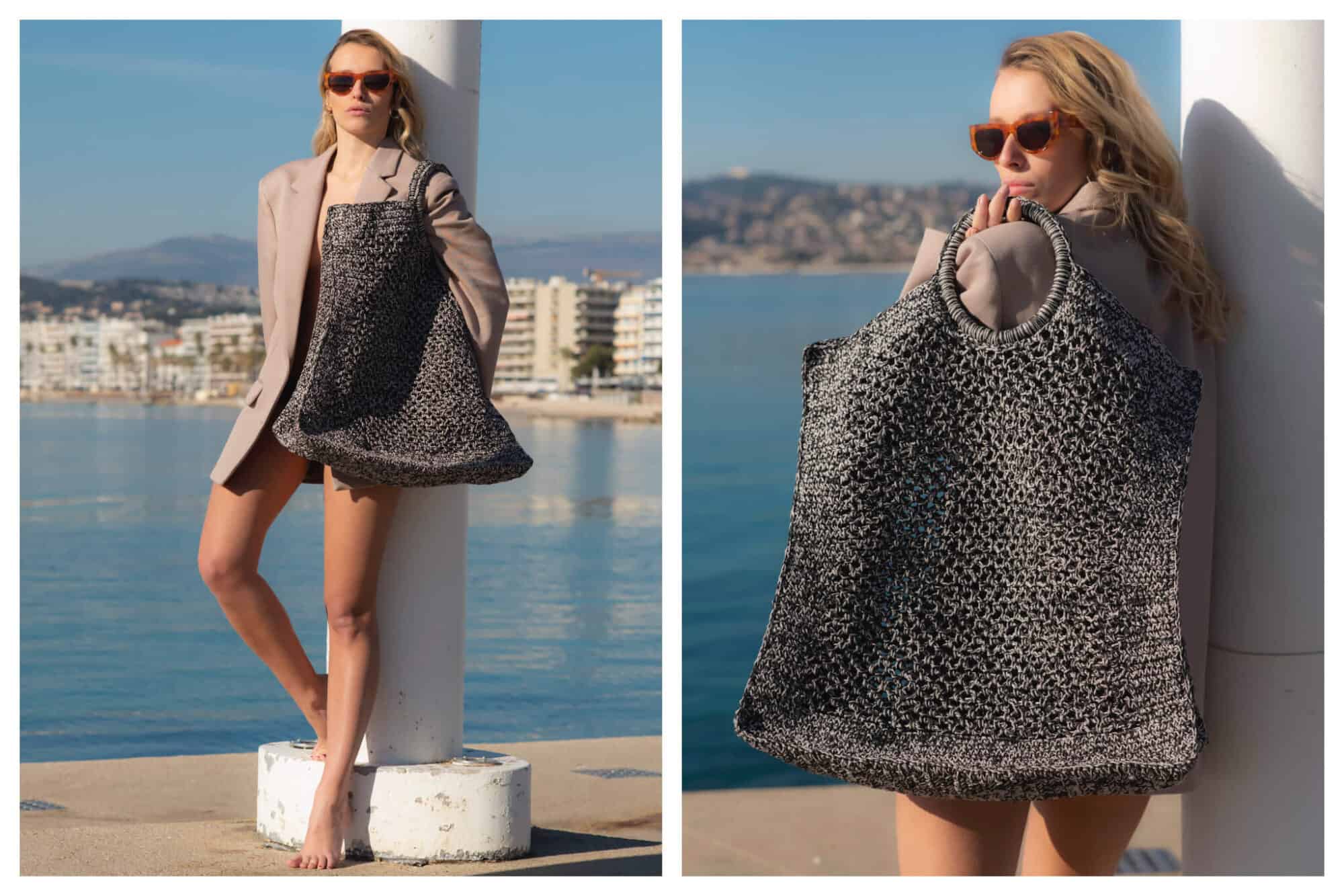 A model in a blazer and red sunglasses models a large bag from Mizele in front of the ocean on a sunny day.