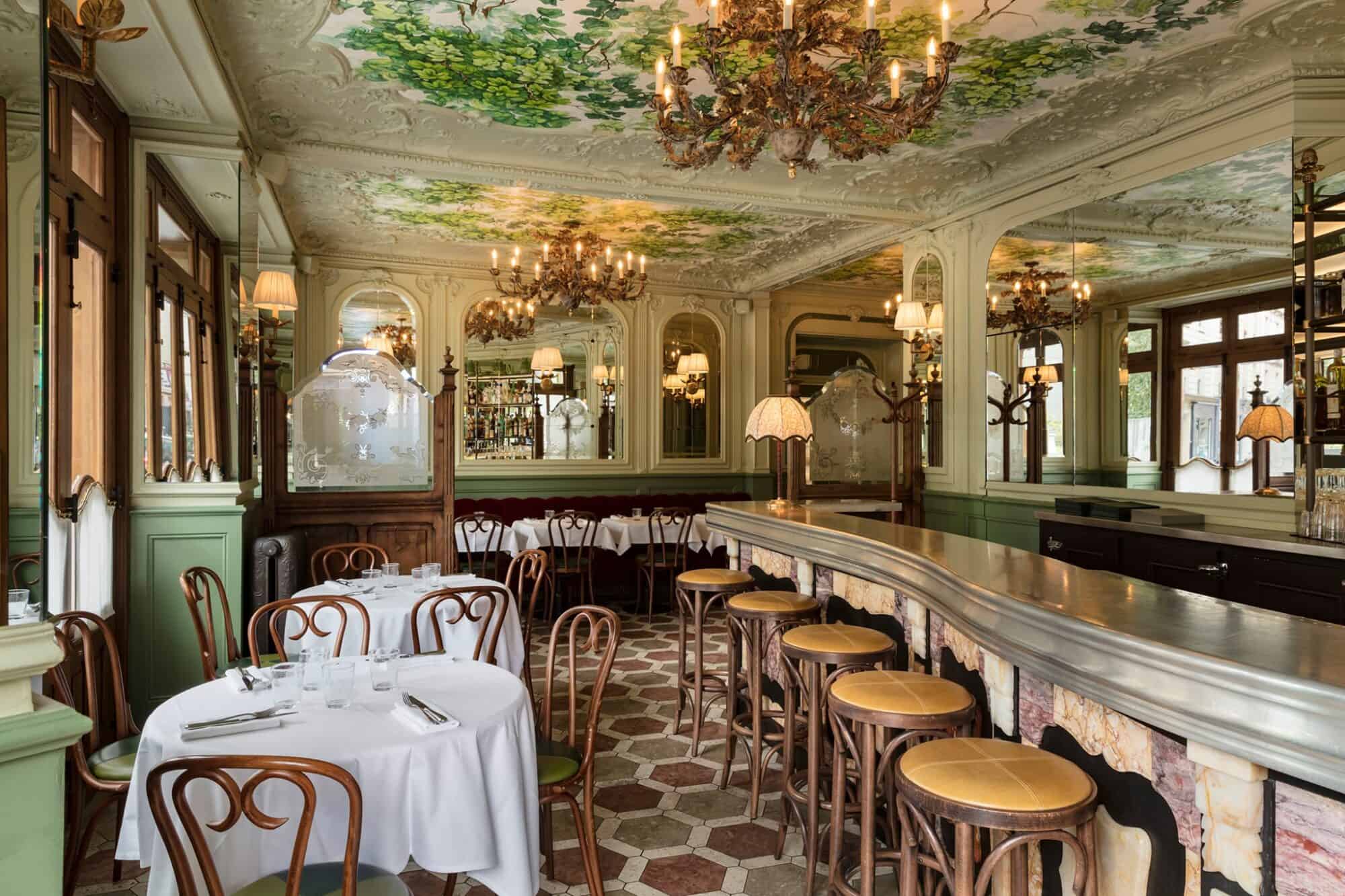 The interior of Le Chardenoux restaurant, decorated with beautiful gold chandeliers and green detailing on the walls and ceiling.