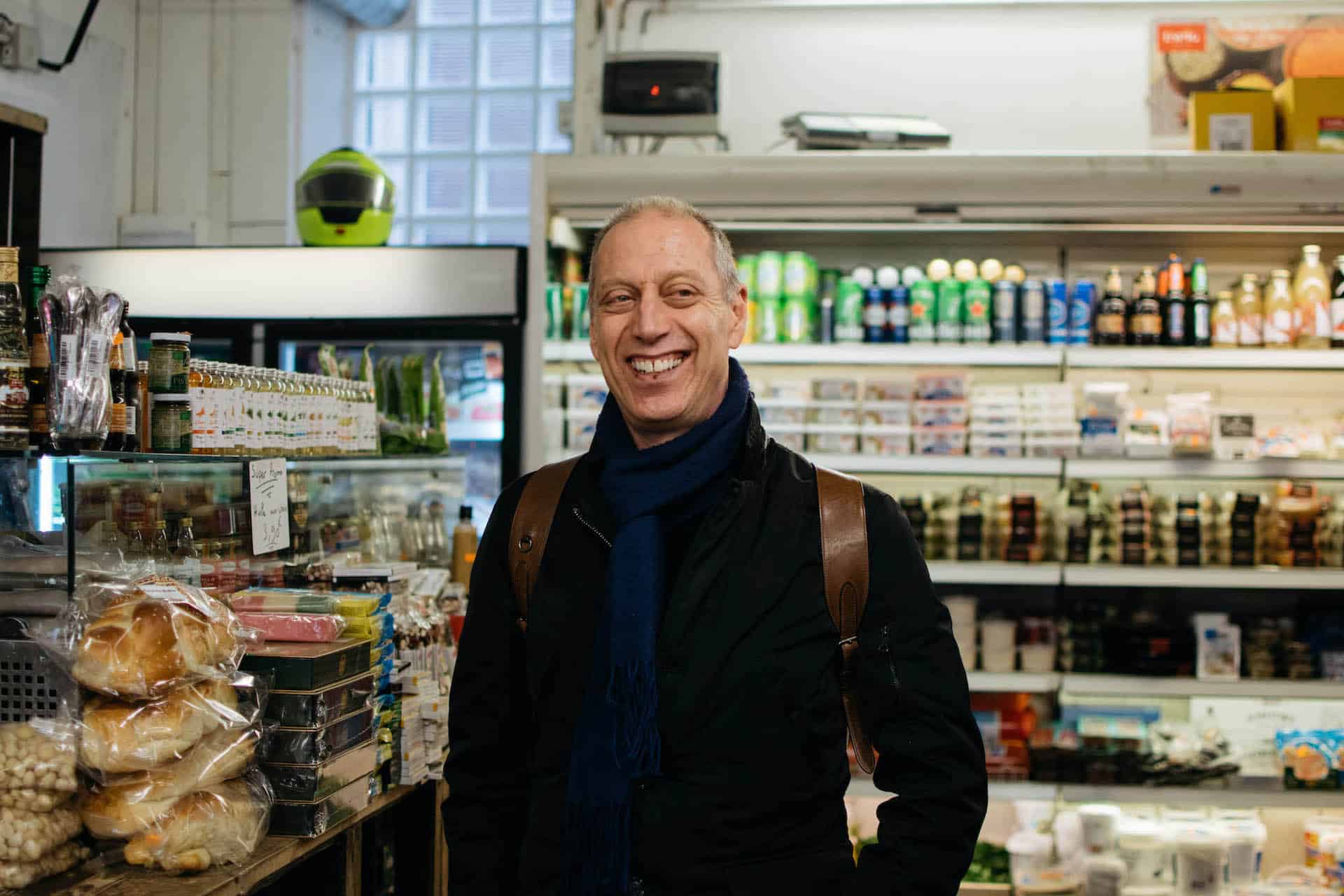 Author David Lebovitz standing in a small grocery store. He is wearing a dark coat and scarf and a brown leather backpack. He has short gray hair and is smiling while looking to the right of the frame.