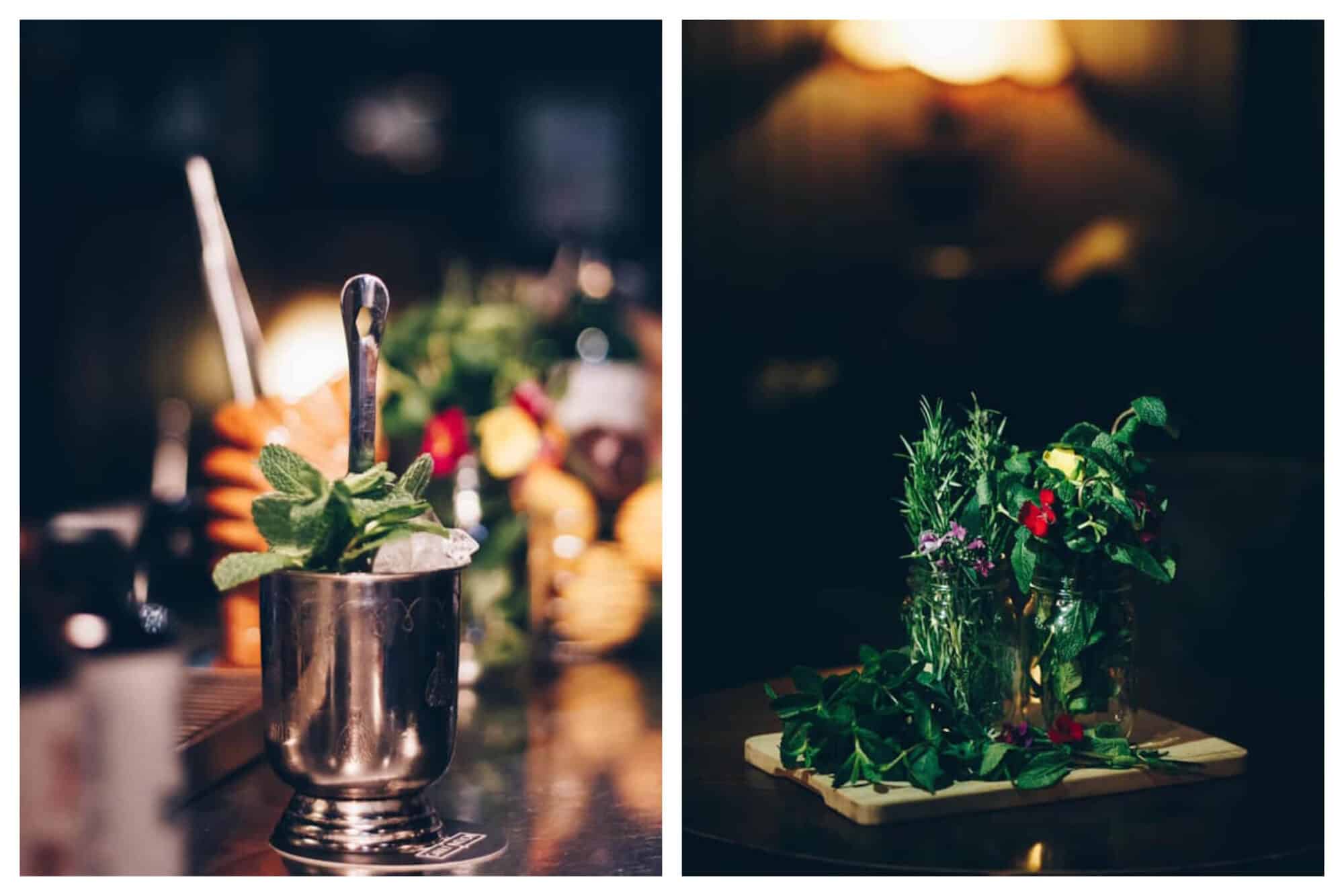 On the left an artfully placed metal cocktail tumbler with ice, a spoon and green garnish. On the right an extravagant cocktail glass with green leaves and red and purple flowers decorating it.
