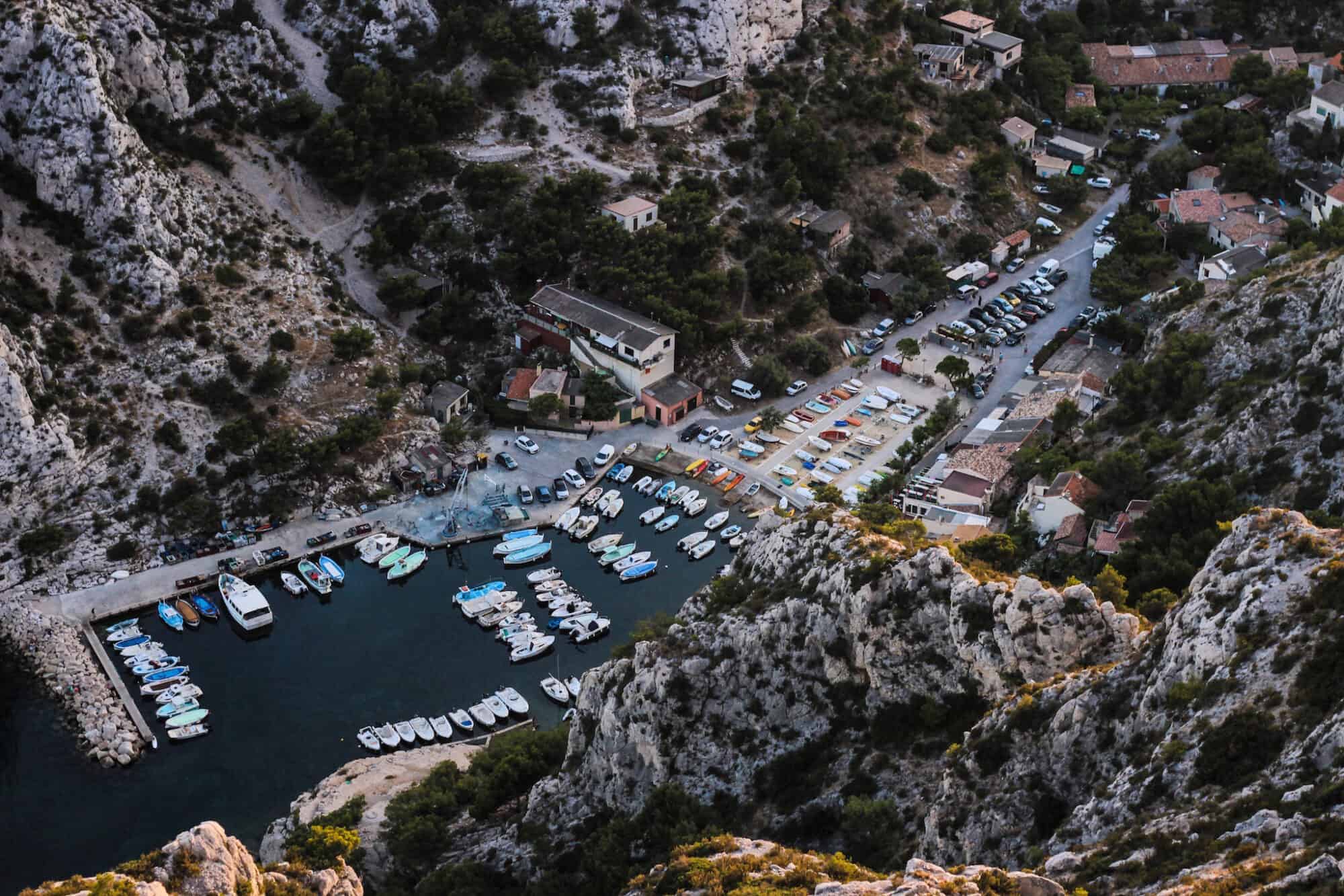 A rocky bay near in the South of France, crowded with small boats and dozens of parked cars next to it.