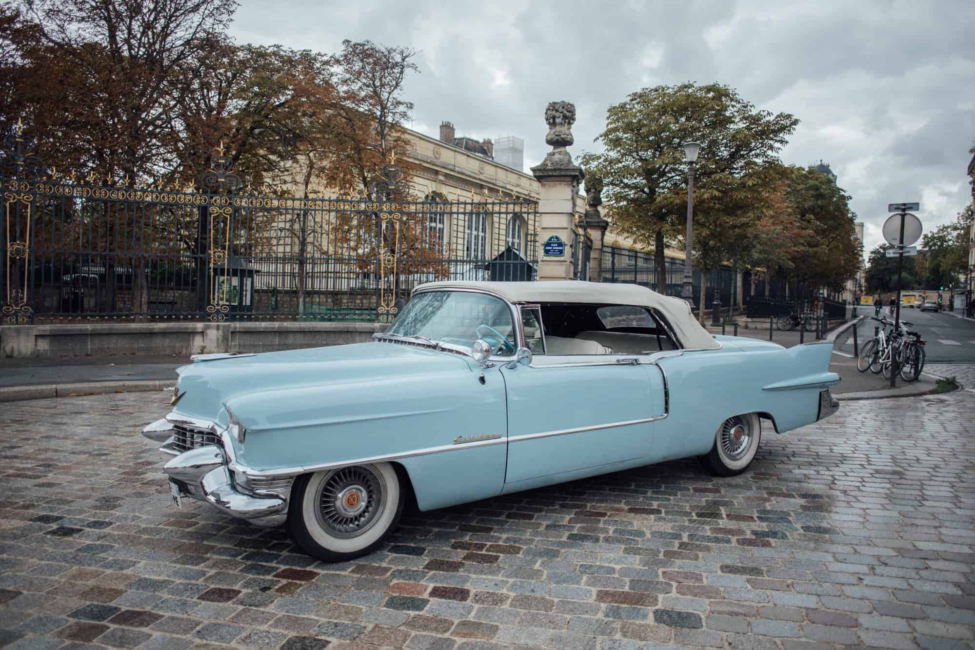 A old blue car is parked on a cobble driveway on a rainy fall day in Paris
