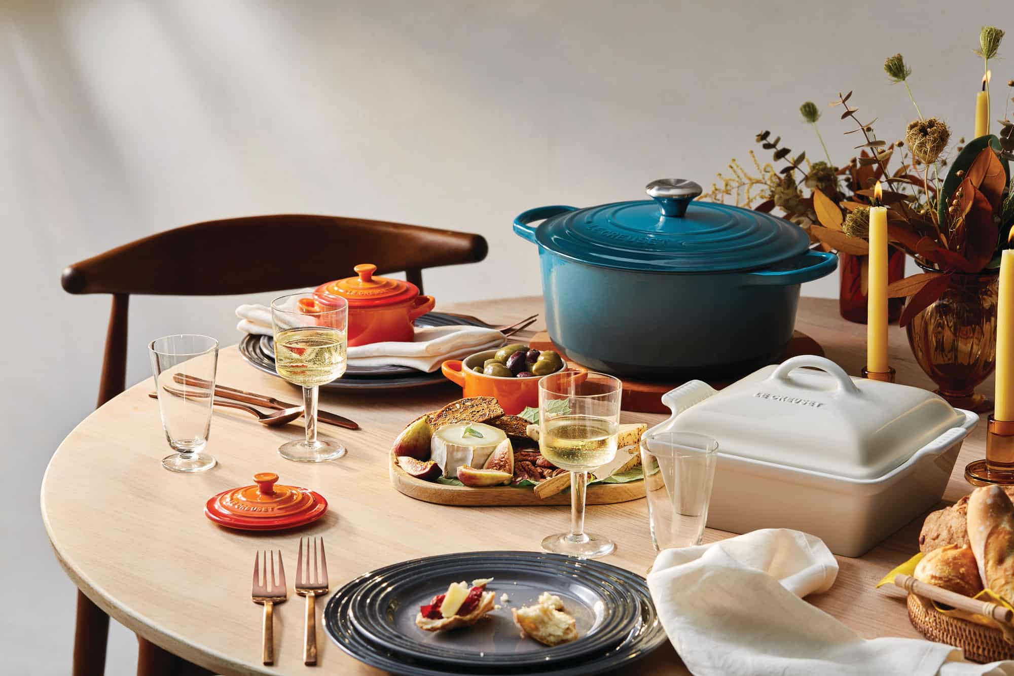 A wooden table with a meal prepared in several Le Creuset pots.