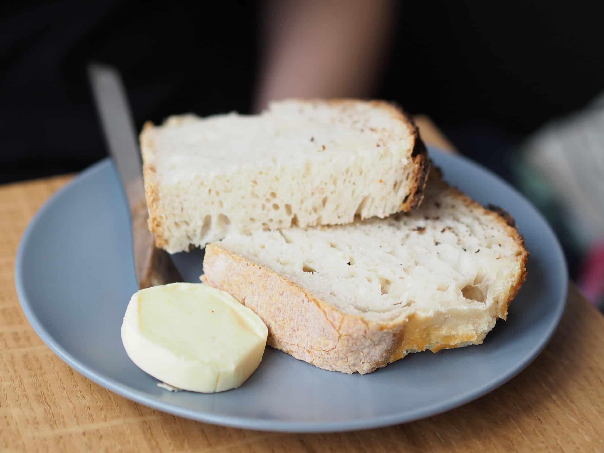 Why does French butter taste so good? Because it's made by hand, and eaten with a loaf of artisanal bread like on this blue plate on a wooden table.