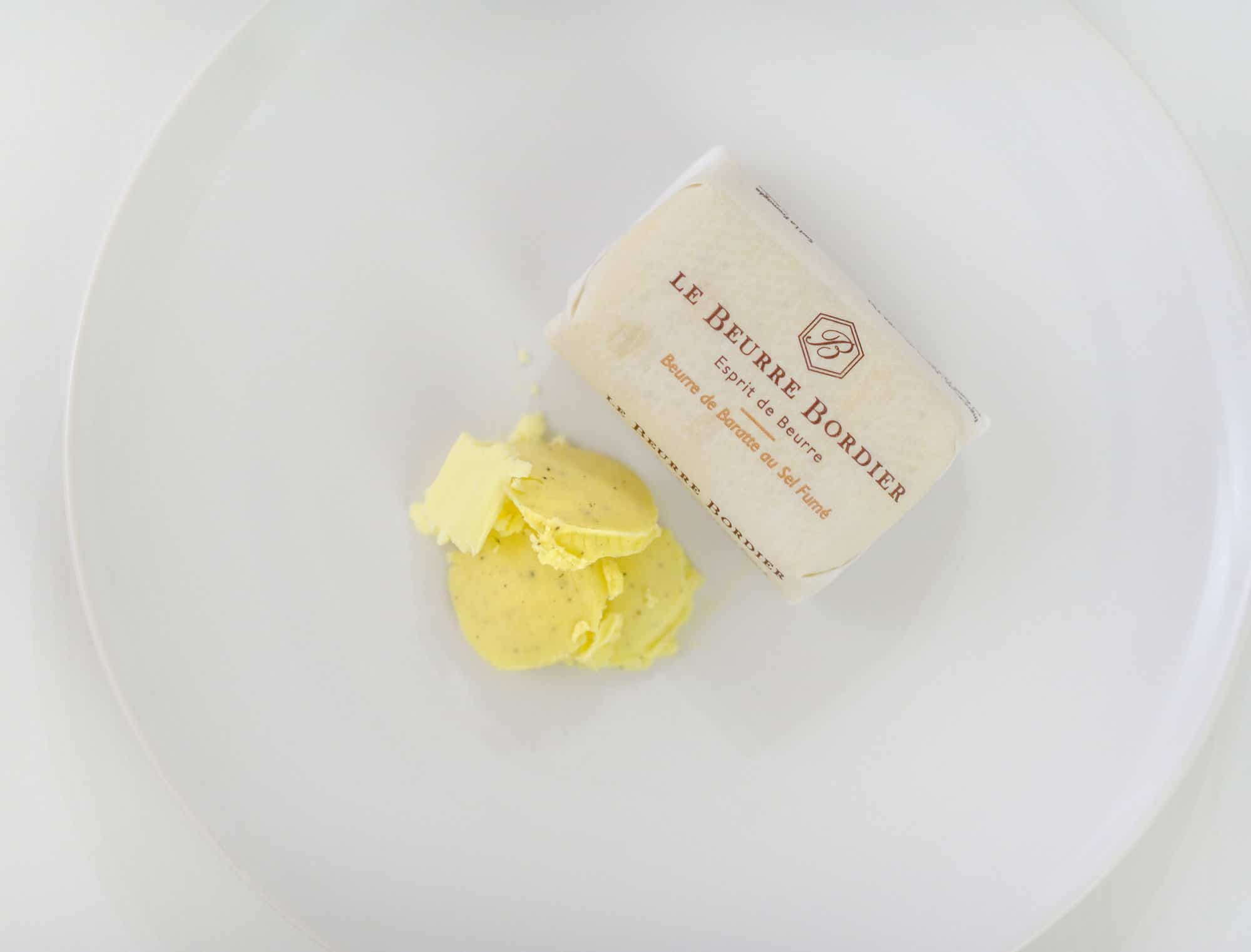 Le Beurre Bordier, a creamy, tasty artisanal butter, resting on top of a white plate.