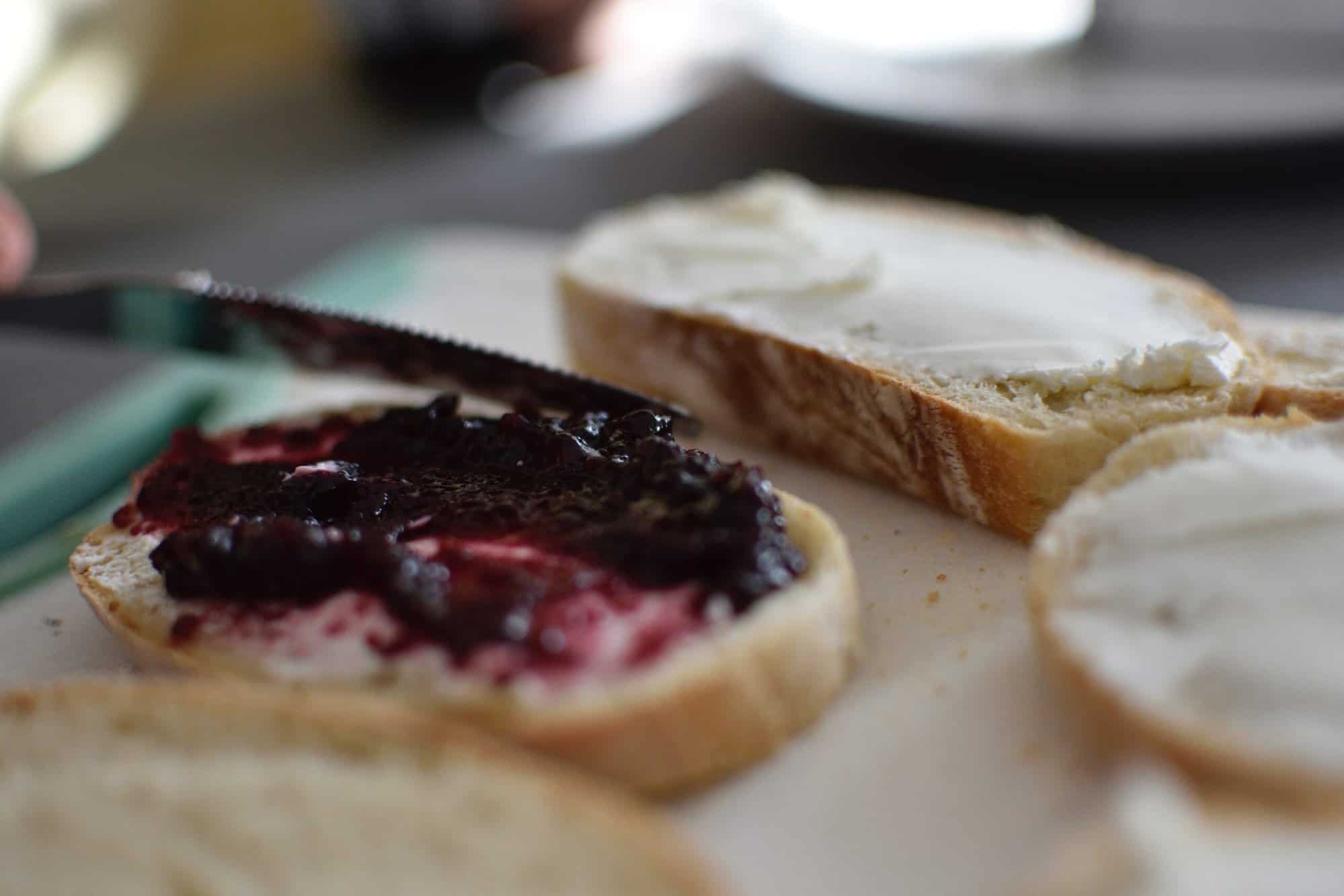 Two pieces of French bread on a cutting board, one with butter on top and the other with butter and berry jam.