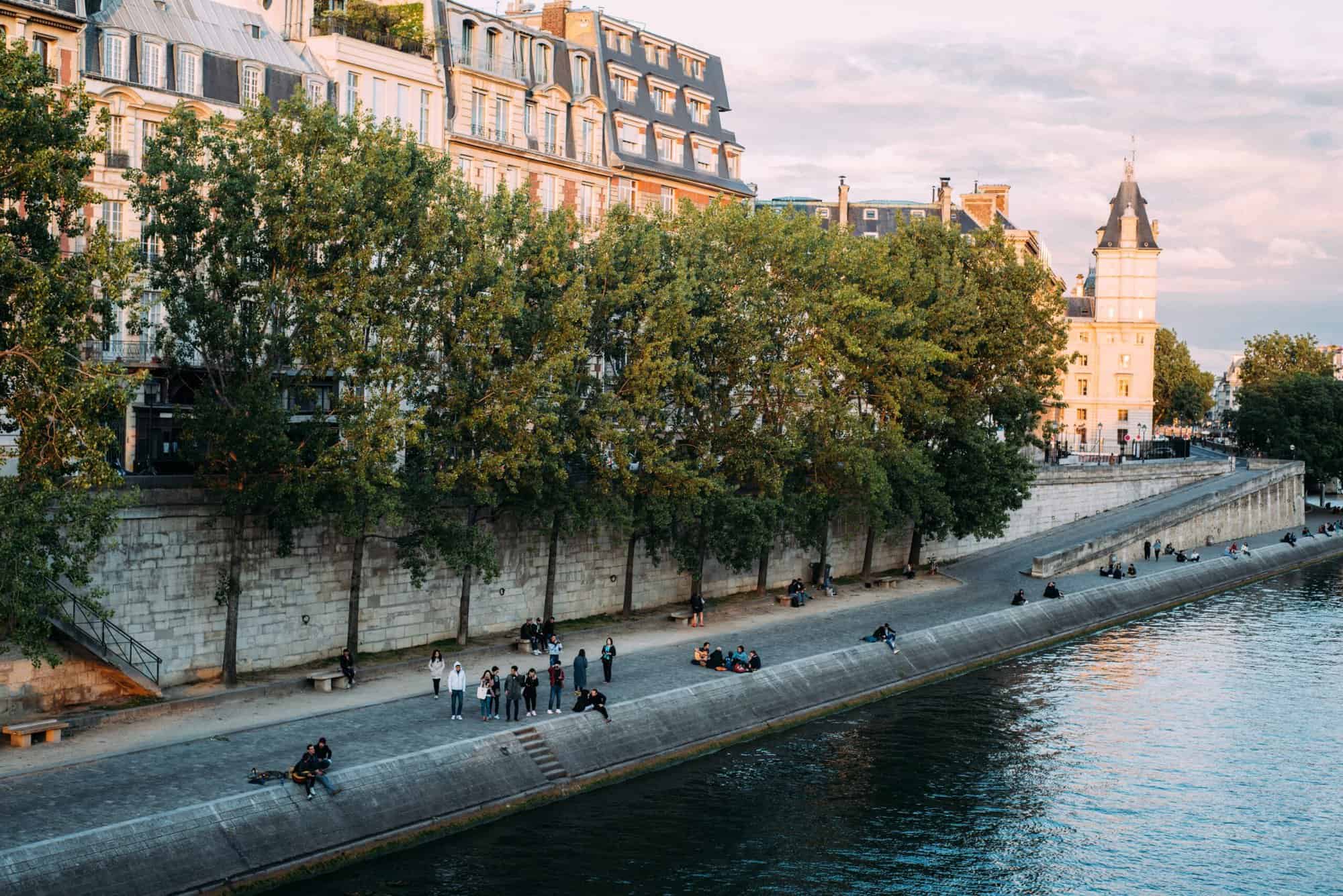 People sit alongside the Seine River in Paris during sunset. 