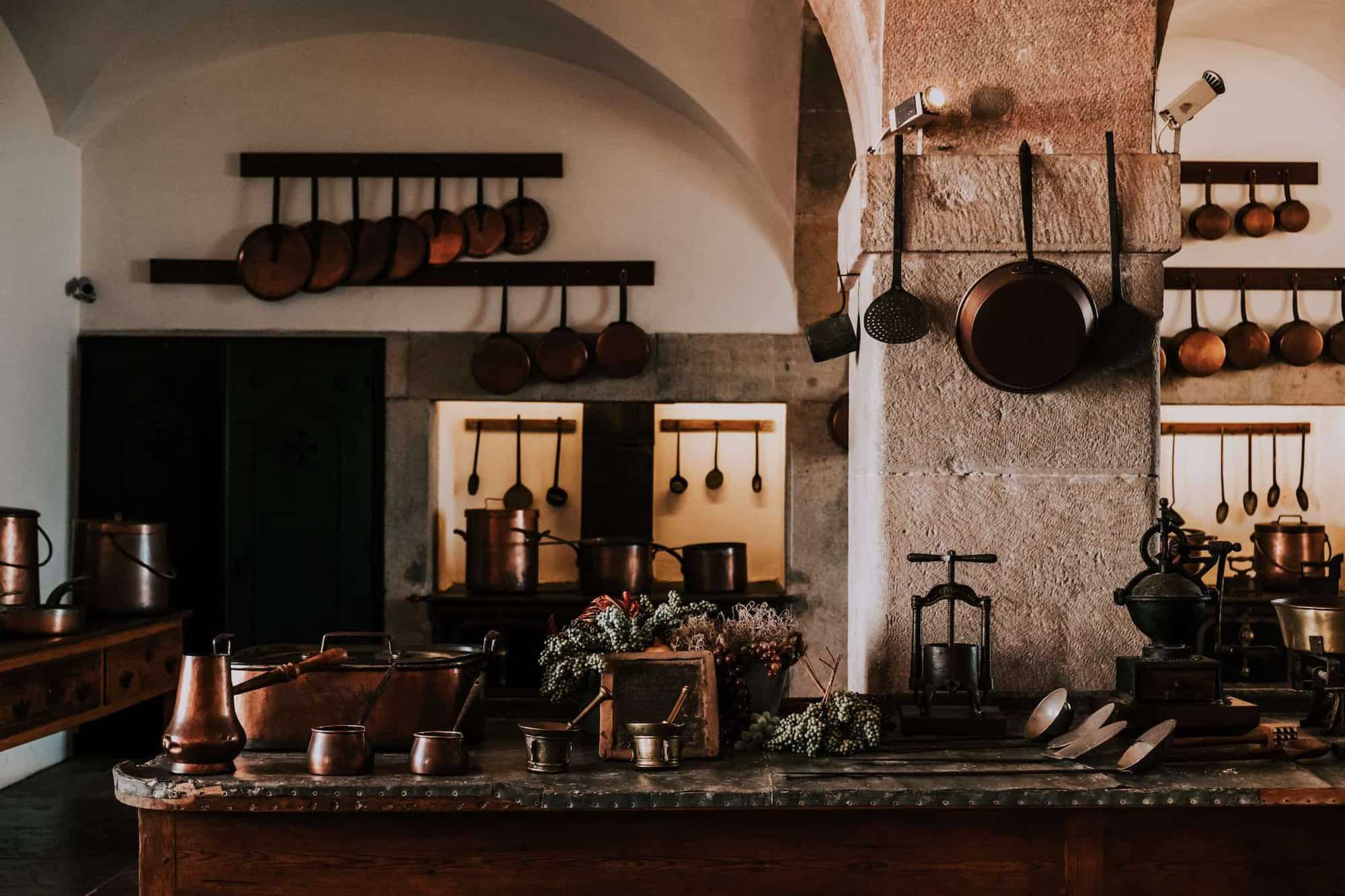 a traditional kitchen with a wooden table. there are many copper utensils neatly organised across the room, pots and cutlery on the table and copper pans hung up on the walls