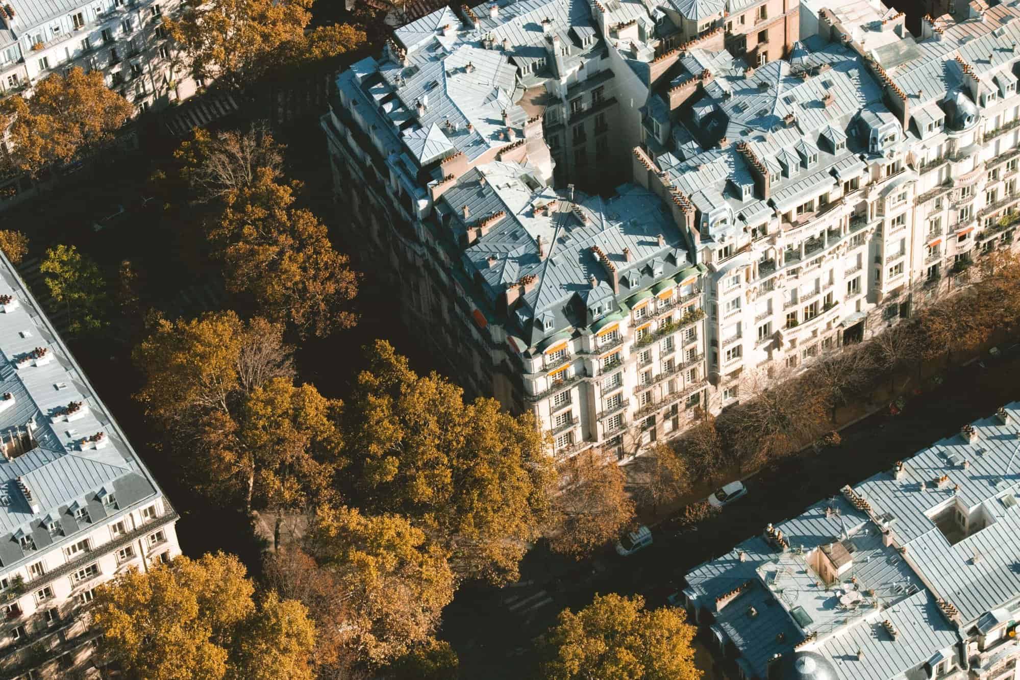 Aerial views of a Parisian street during autumn, overlooking trees and buildings, and the famous Parisian zinc rooftops.