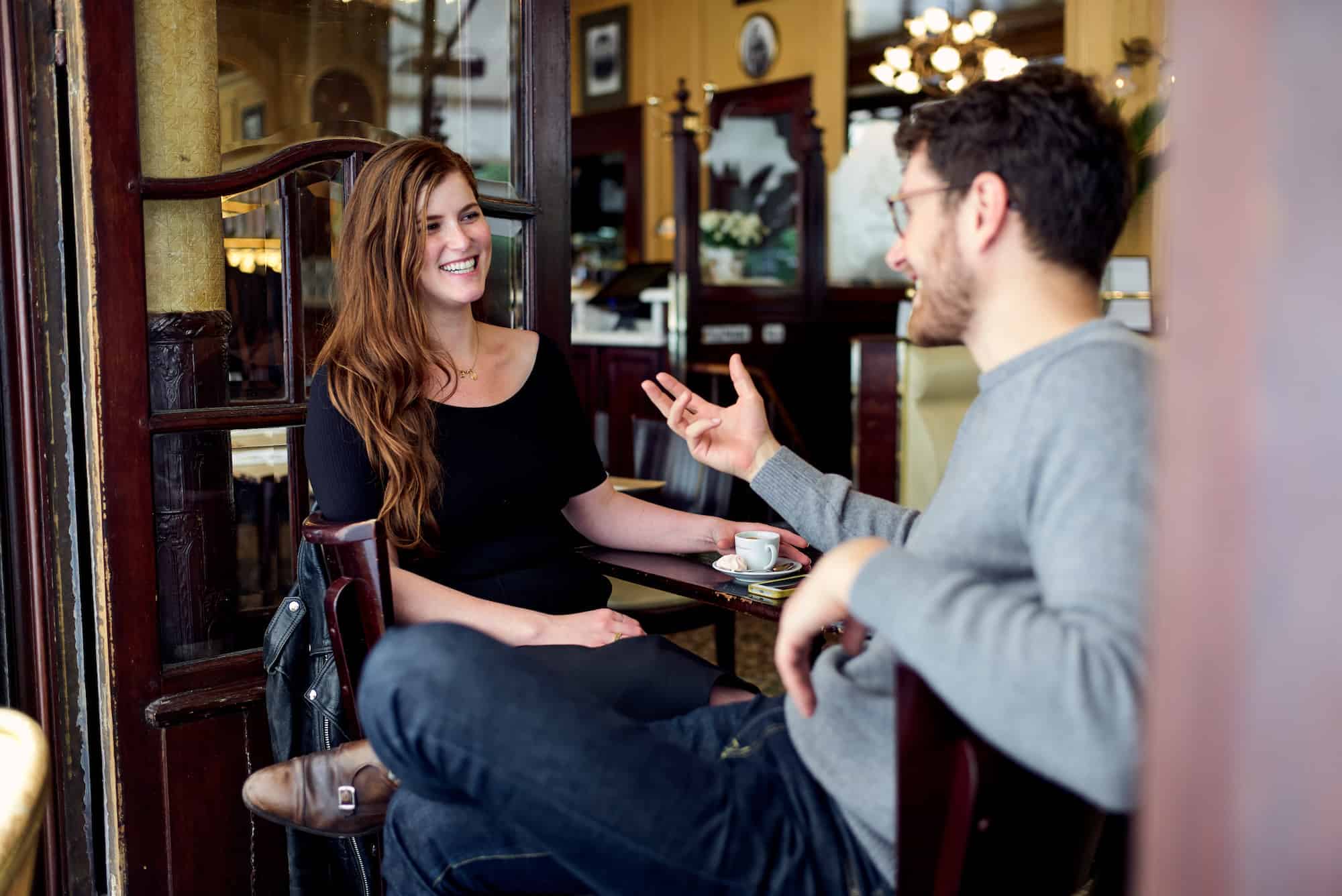 A man and woman sit laughing at a cafe table.