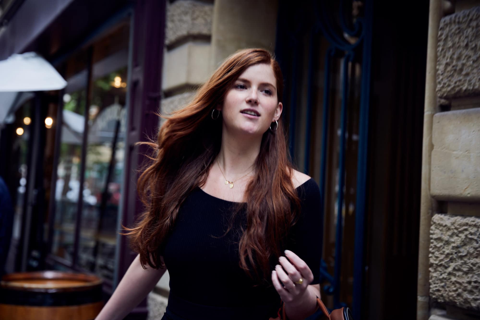 A redheaded woman in a black shirt is walking out of a Parisian bistrot.