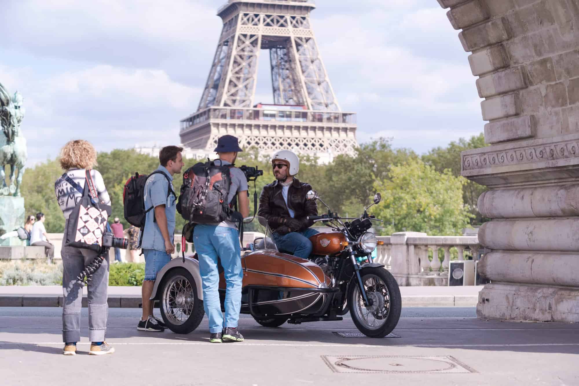 Simon Burke on his motorbike talking to passersby near the Eiffel Tower on a grey day in Paris. 