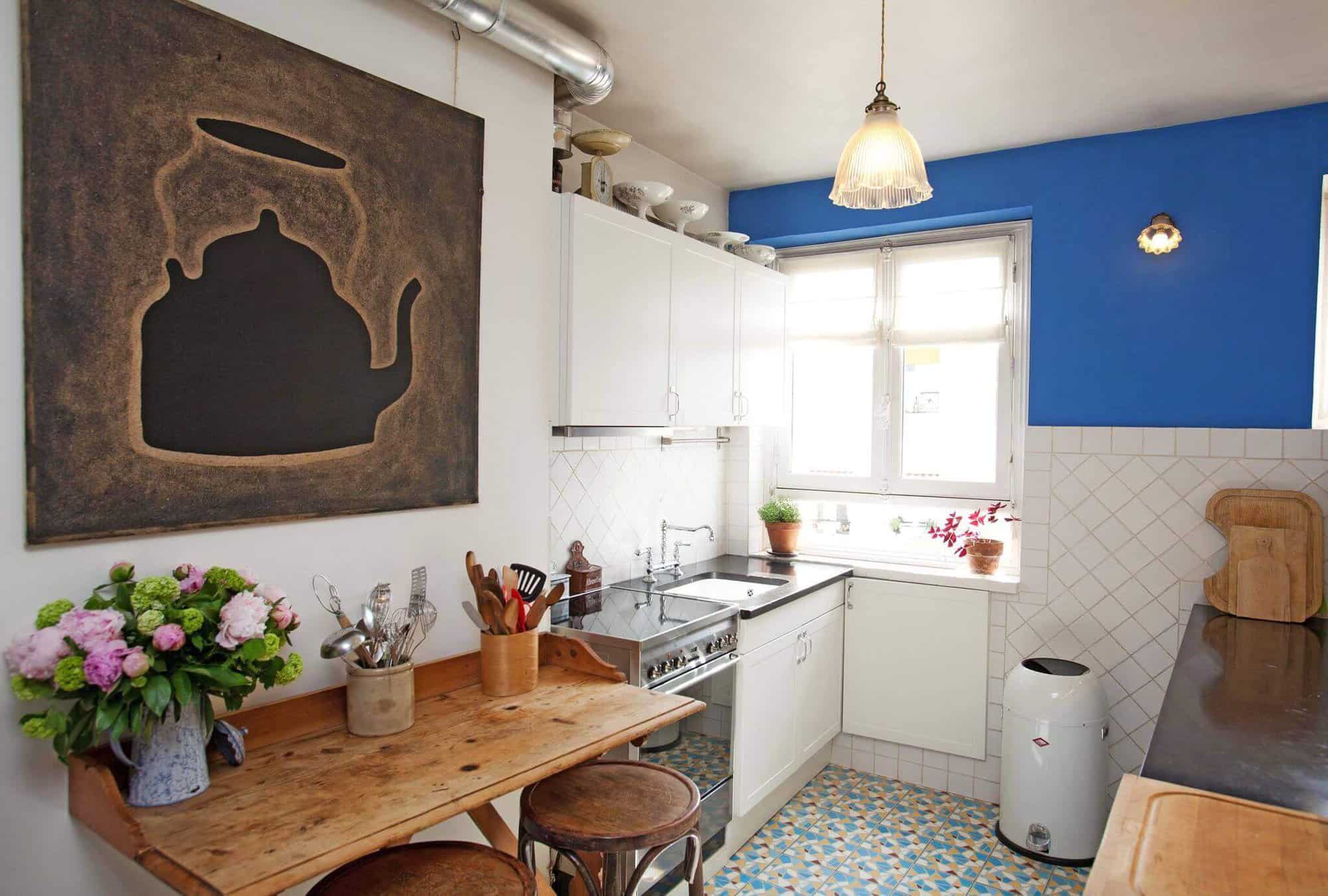 A breakfast bar with wooden stools sits to the left of a silver oven in inside a blue and white kitchen 