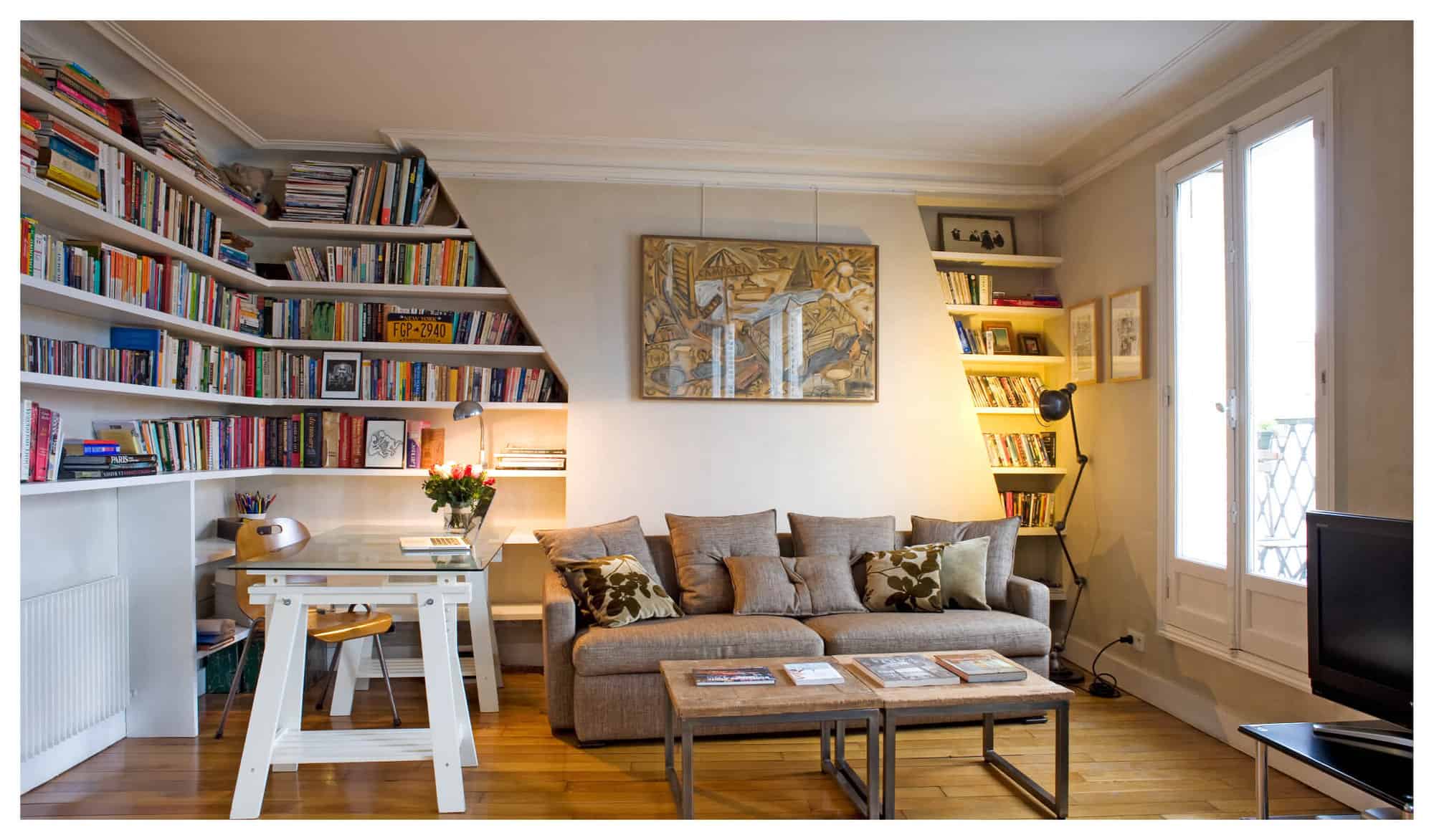 A large beige sofa and desk sit inside a Parisian salon that's filled with several bookshelves