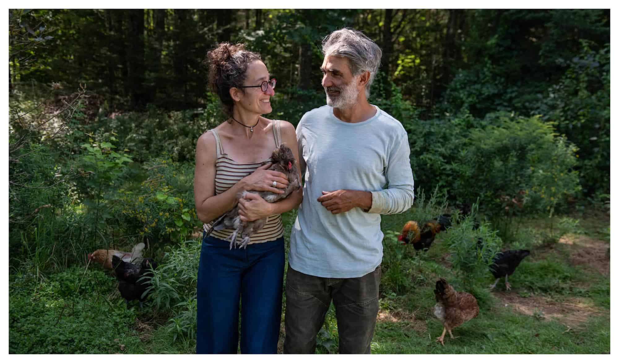 Veggies to Table founder Erica Berman holds a chicken in her arms while smiling and looking at her husband Alain on their farm in rural Maine.