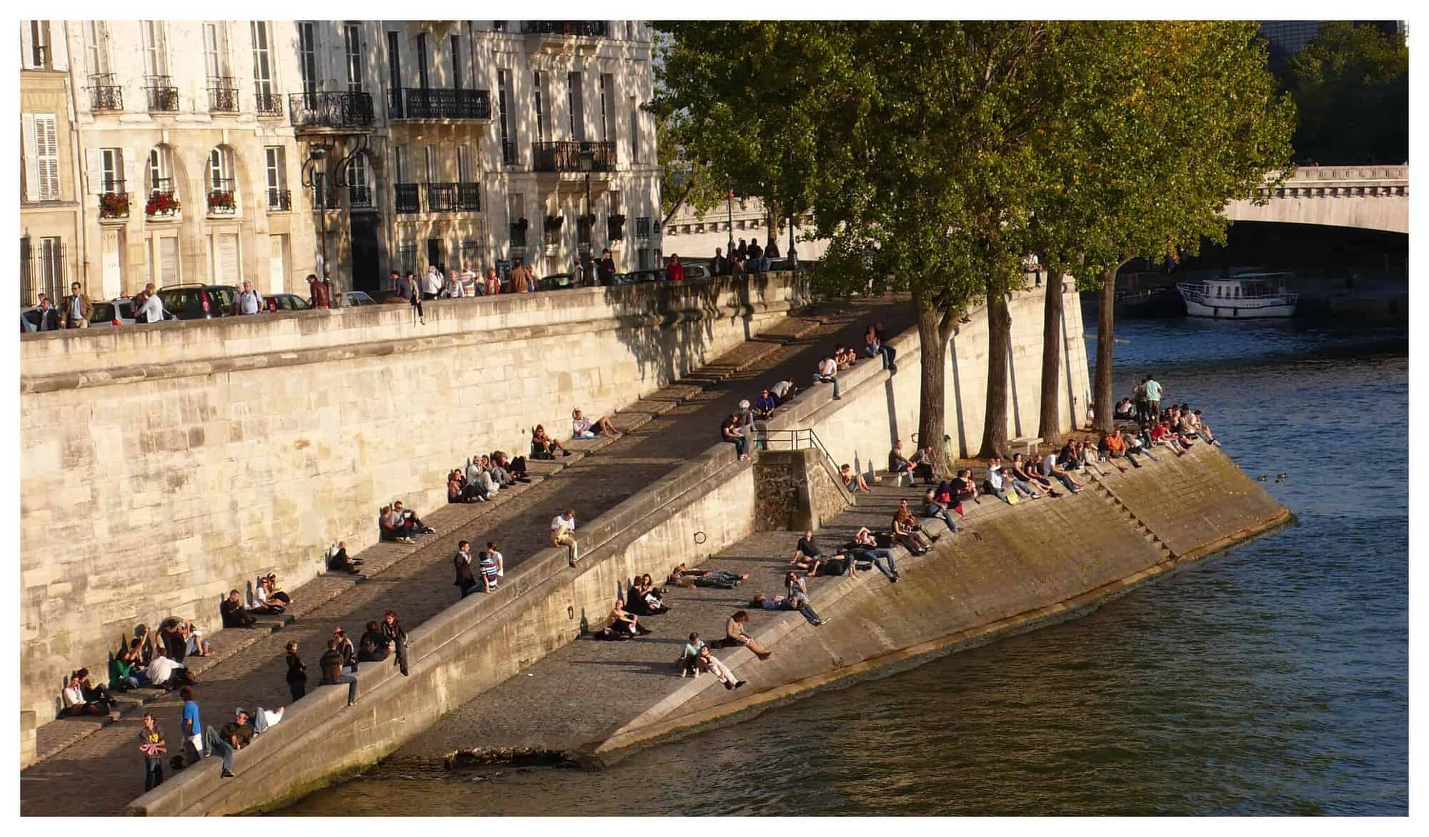 People hanging out by Paris's Seine river during a sunset.