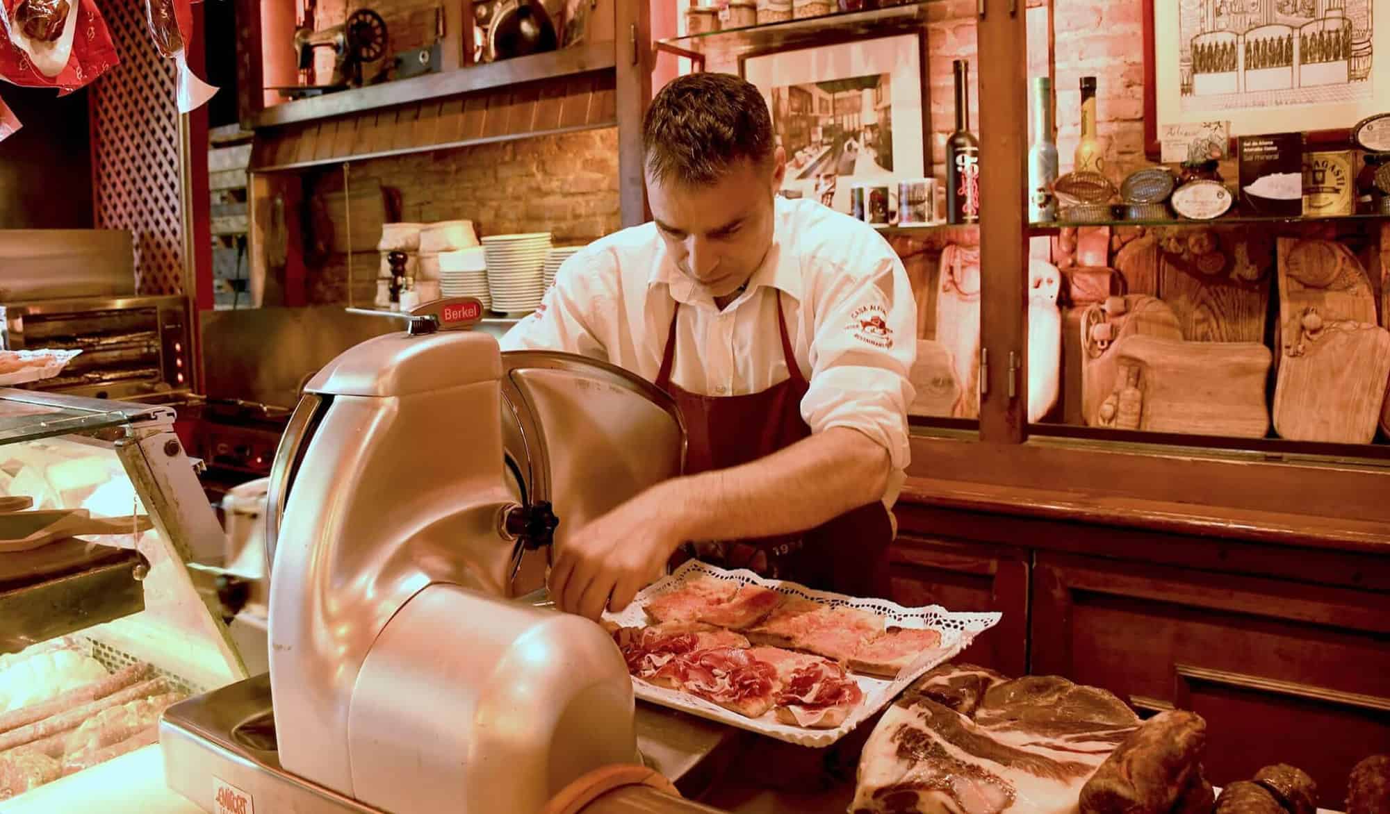 A man with a red apron slices dried ham at Casa Alfonso.